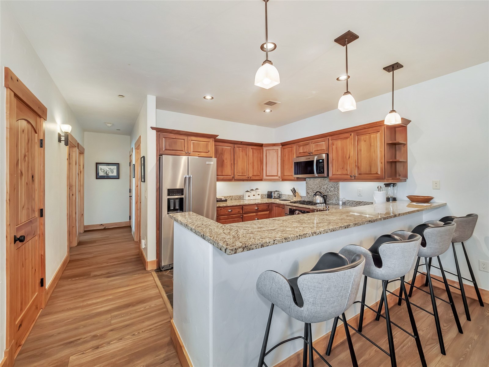 Kitchen with warm wood cabinets, granite breakfast bar, and upholstered bar stools.