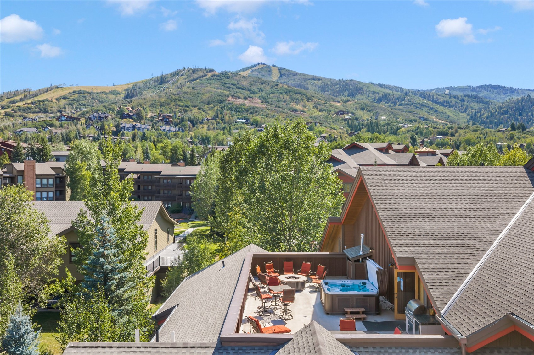 Rooftop deck with a hot tub and fire pit overlooking green mountains.