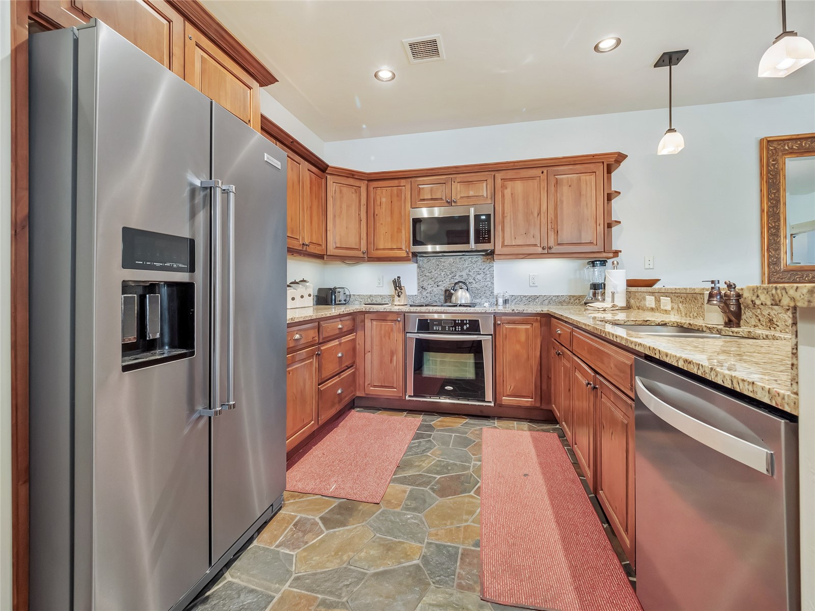 Kitchen with warm wood cabinetry, granite counters, stainless steel appliances, and stone tile flooring.