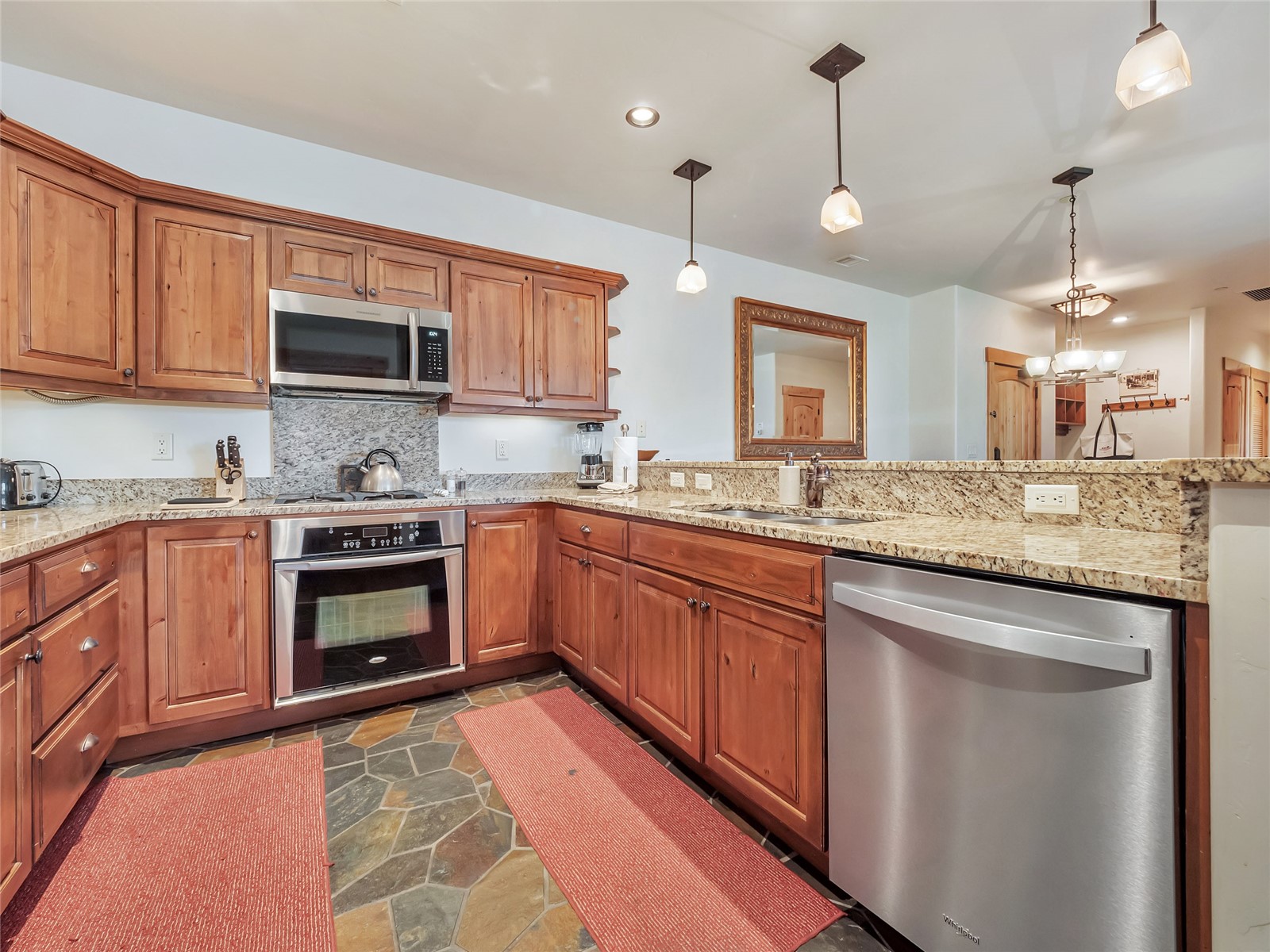 Kitchen with wood cabinetry, granite counters, stainless steel appliances, and slate tile flooring.