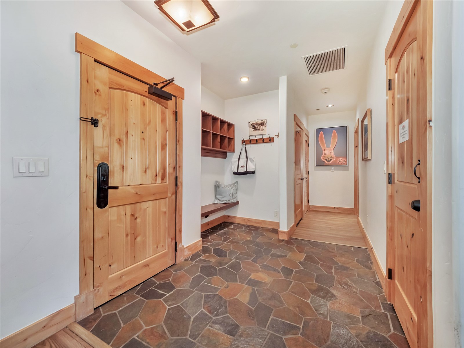 Entryway with rustic wood doors, slate flagstone flooring, and a built-in bench with coat storage.