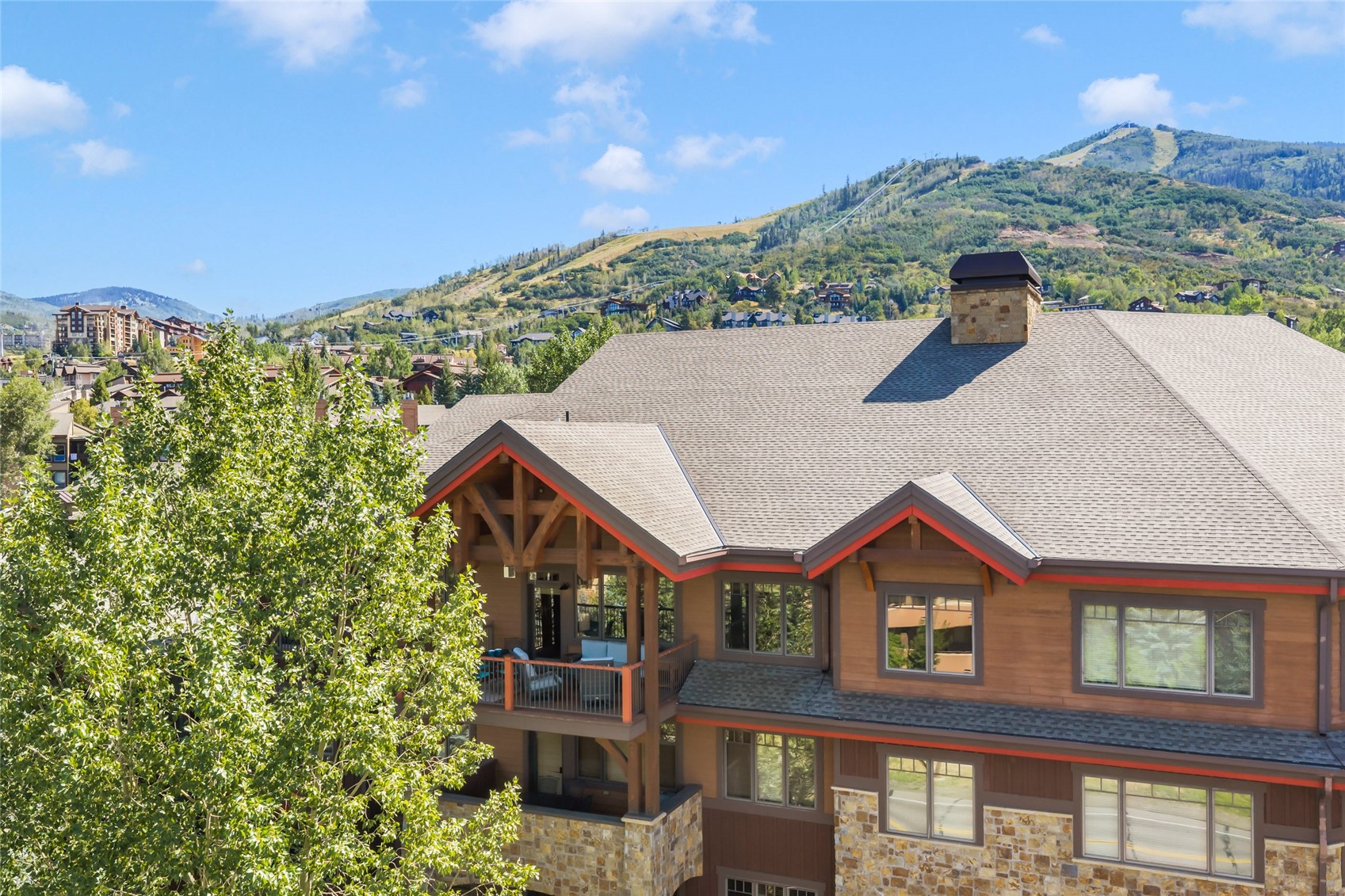 Mountain-style home with stone accents and red roof trim against a green mountainside.