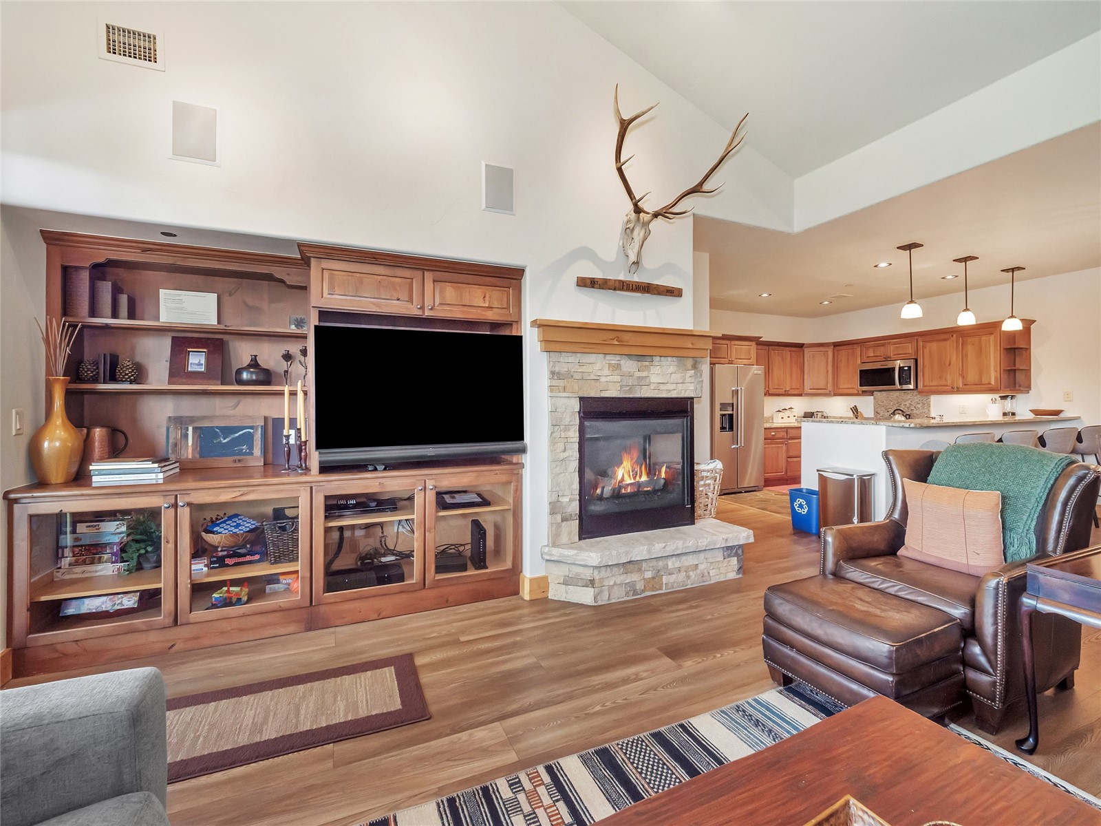 Living room with a stone fireplace, built-in entertainment center, and open kitchen.