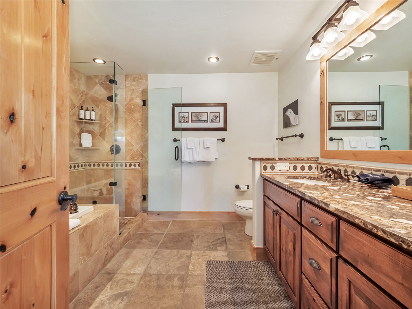 Bathroom with a glass-enclosed tiled shower and long wood vanity with stone countertop.