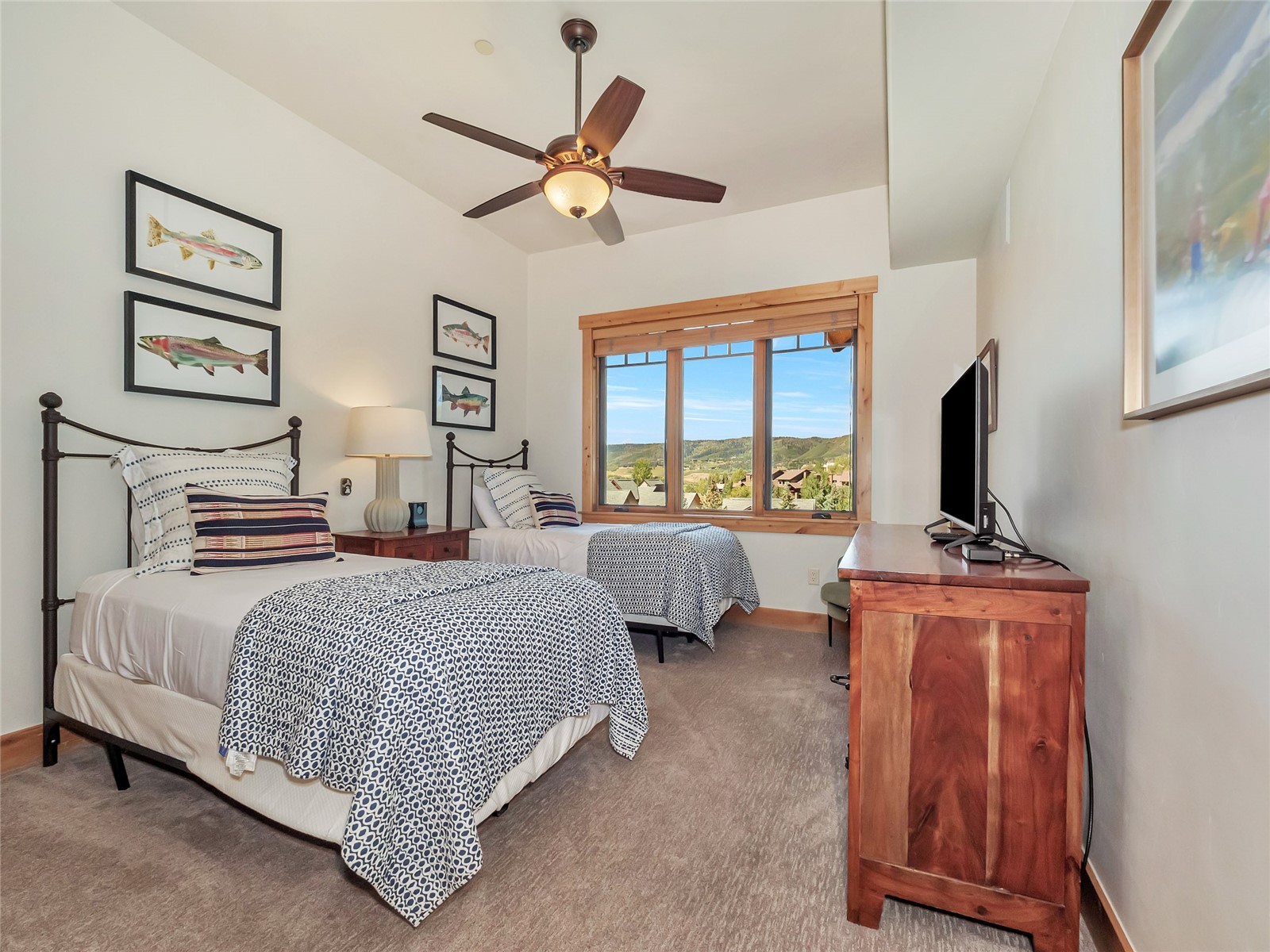 Twin bedroom with patterned bedding, framed fish prints, and a window overlooking green hills.