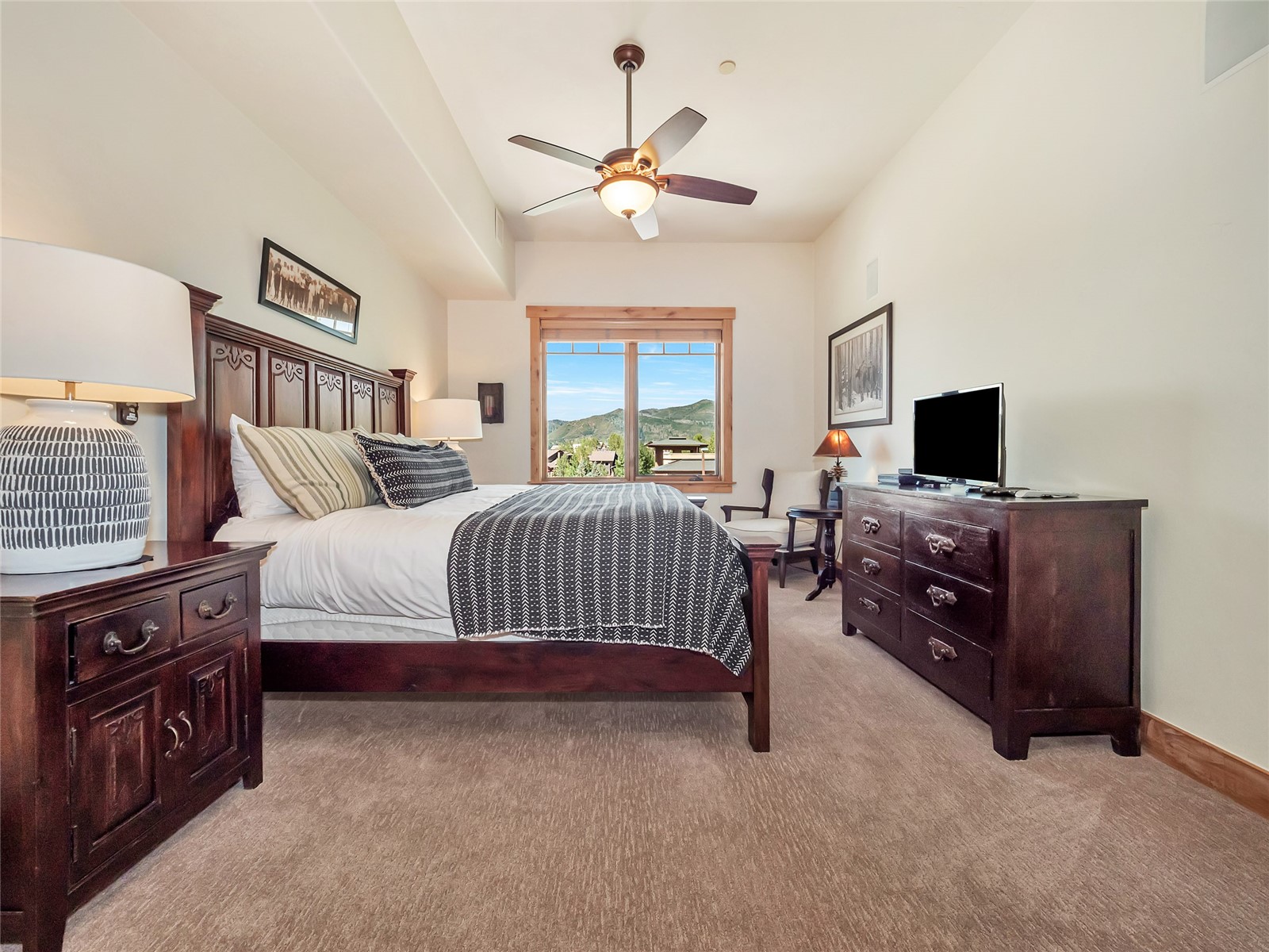 Furnished bedroom with dark wood furniture and a window overlooking green mountains.