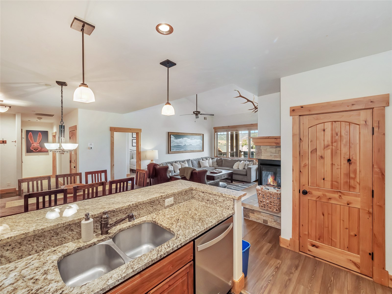 Open-plan kitchen and living room with granite counters, wood cabinetry, and a stone fireplace.