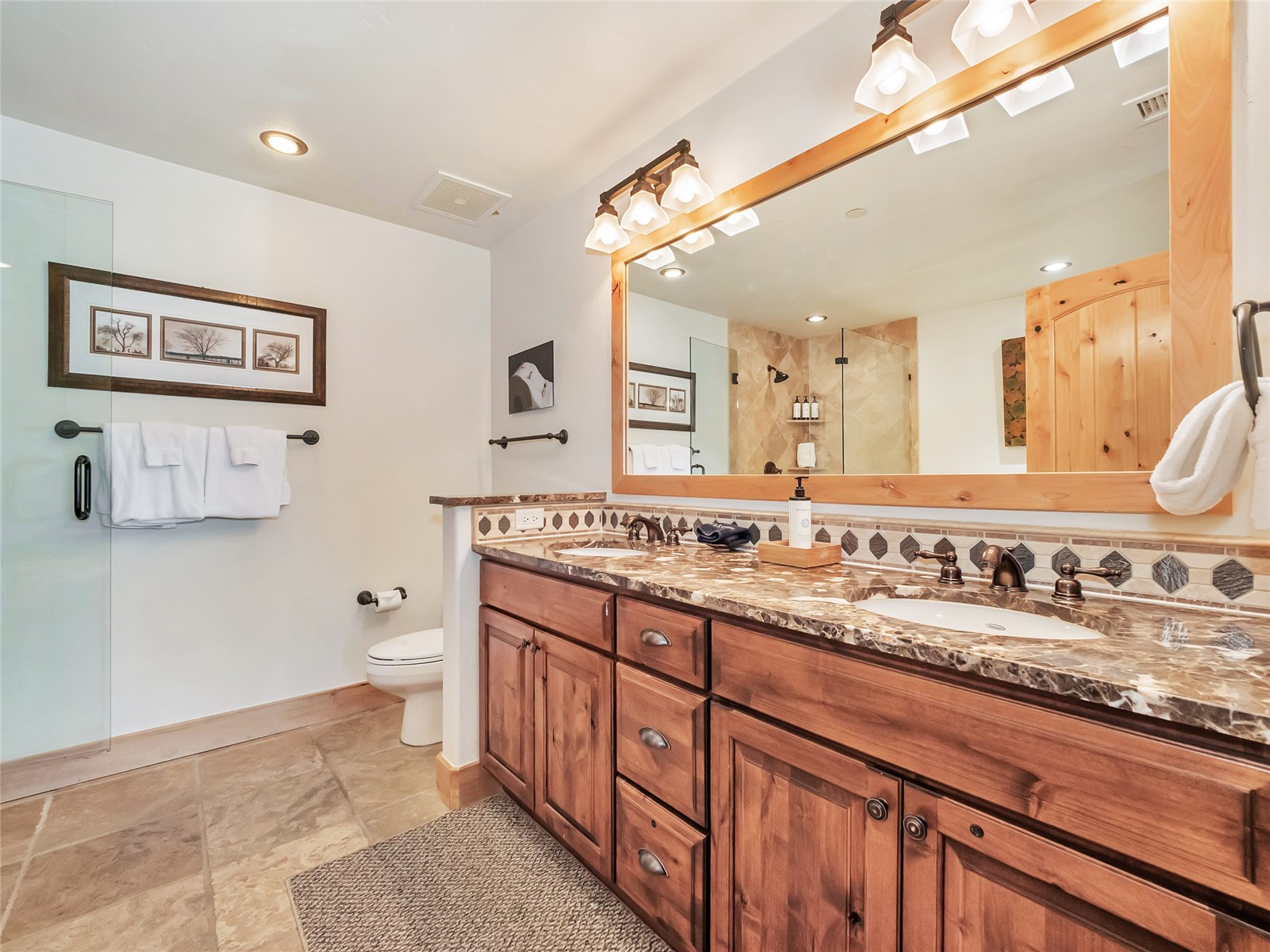 Bathroom with a long wood double vanity, stone countertop, and glass-enclosed shower.
