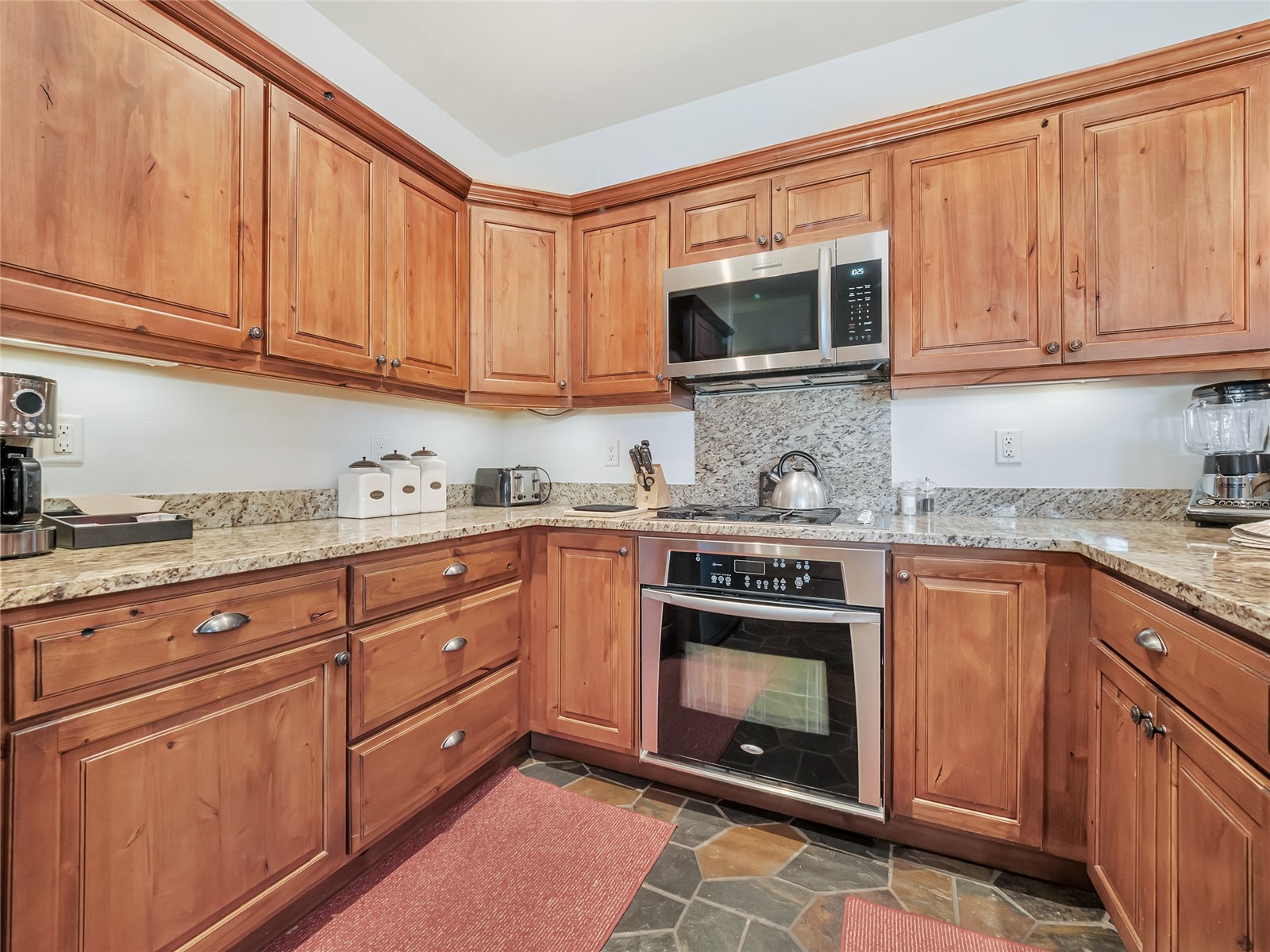 Kitchen with warm wood cabinets, stone counters, and stainless steel appliances.