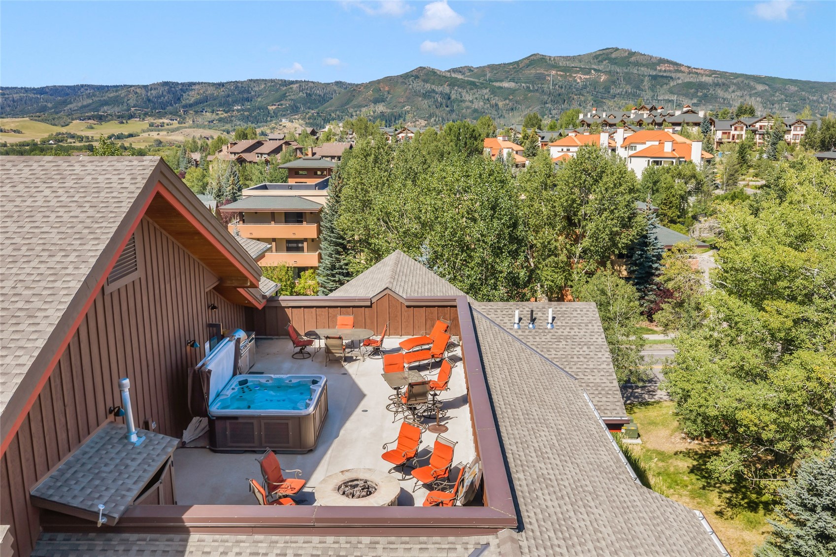 Rooftop deck with a hot tub, fire pit, orange lounge chairs, and mountain views.