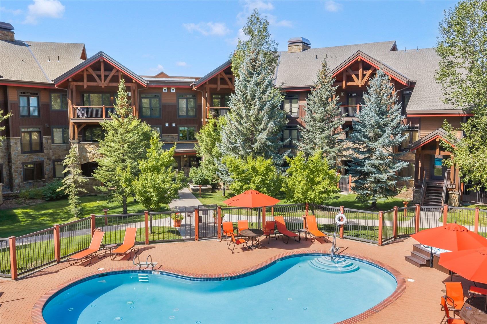 Outdoor pool and patio with orange lounge chairs in front of a multi-story condominium building.