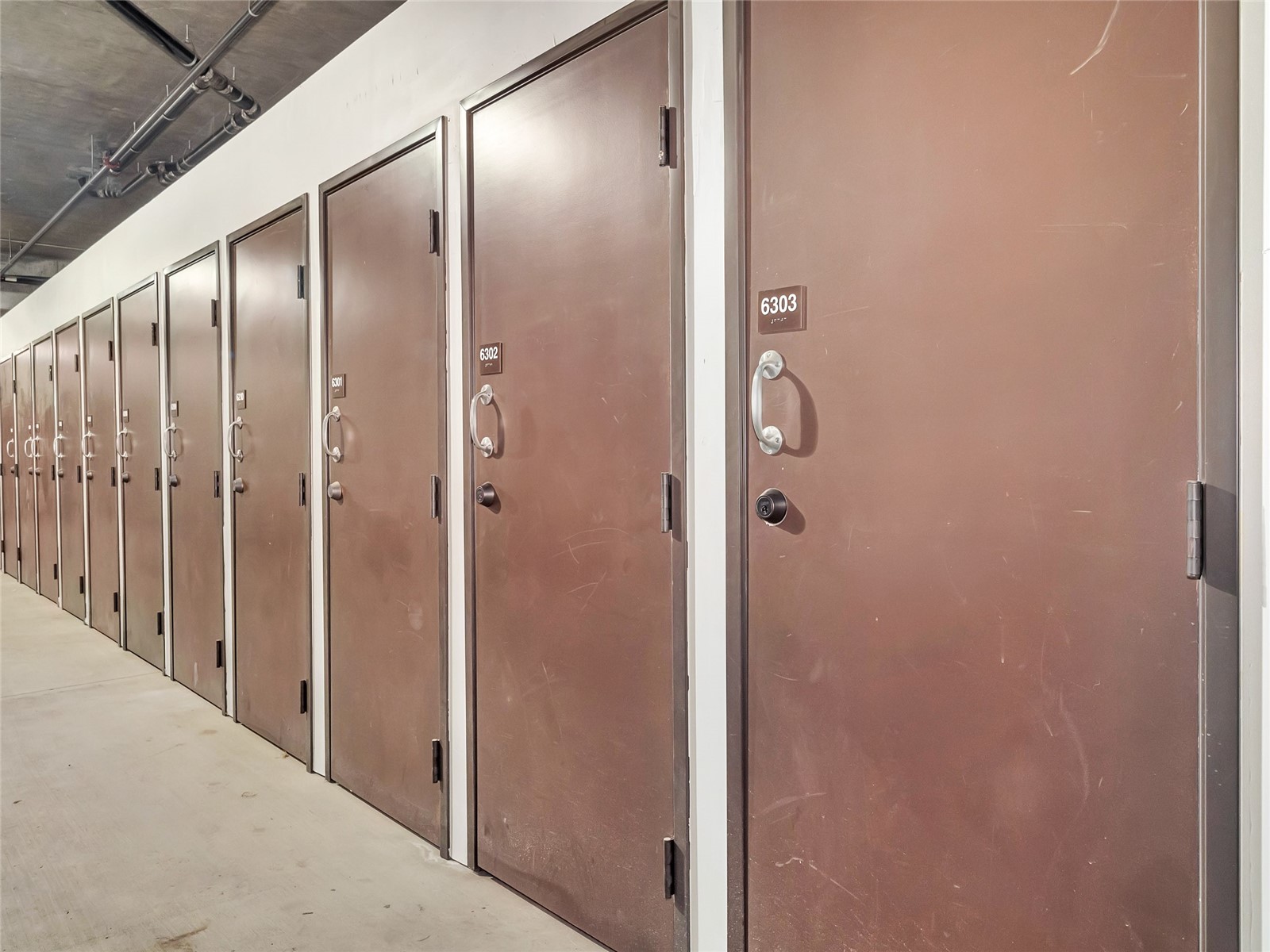Storage corridor lined with brown unit doors; the nearest door is numbered 6303.