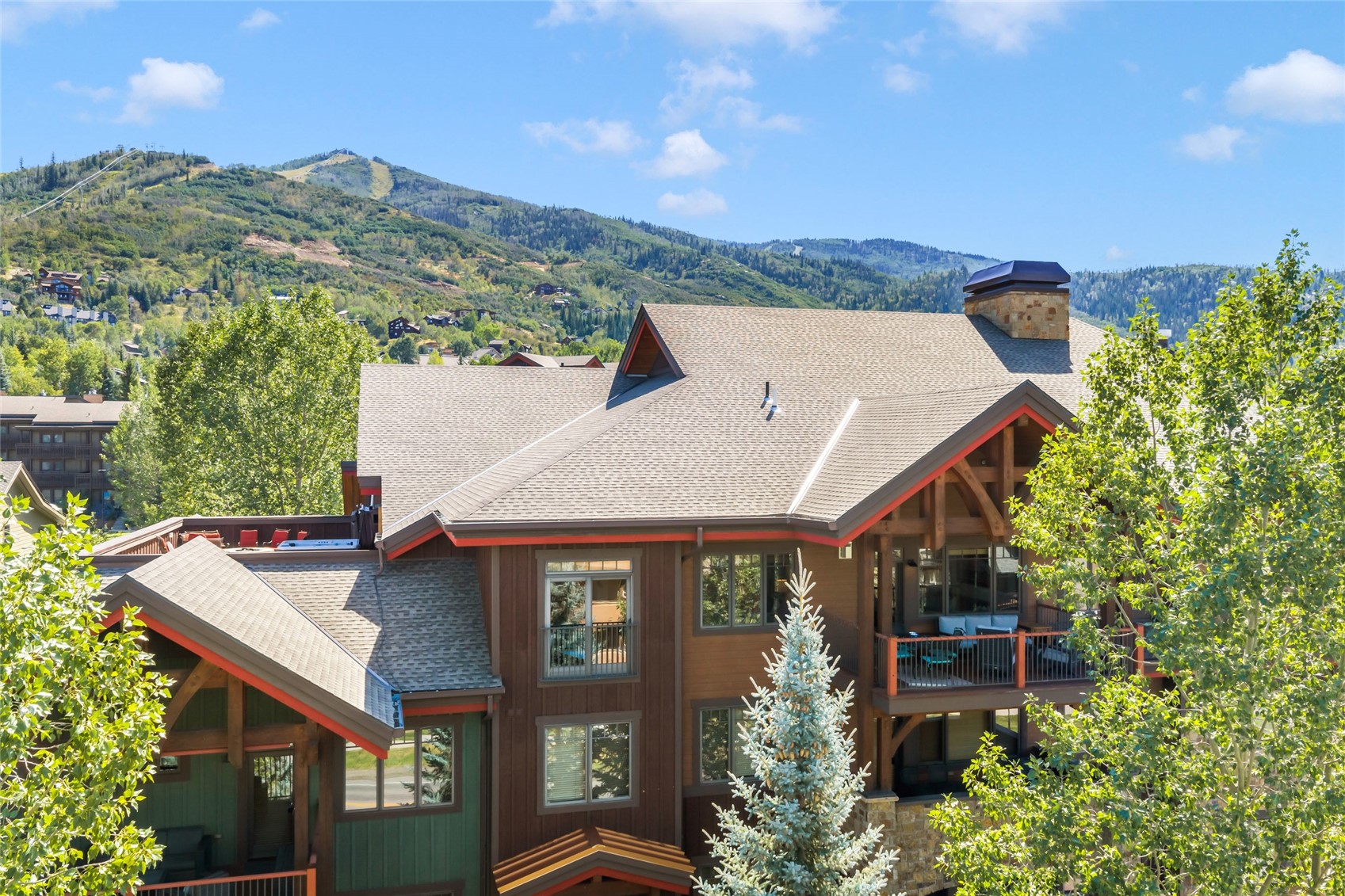 Mountain home with a covered balcony, framed by leafy trees and forested slopes.