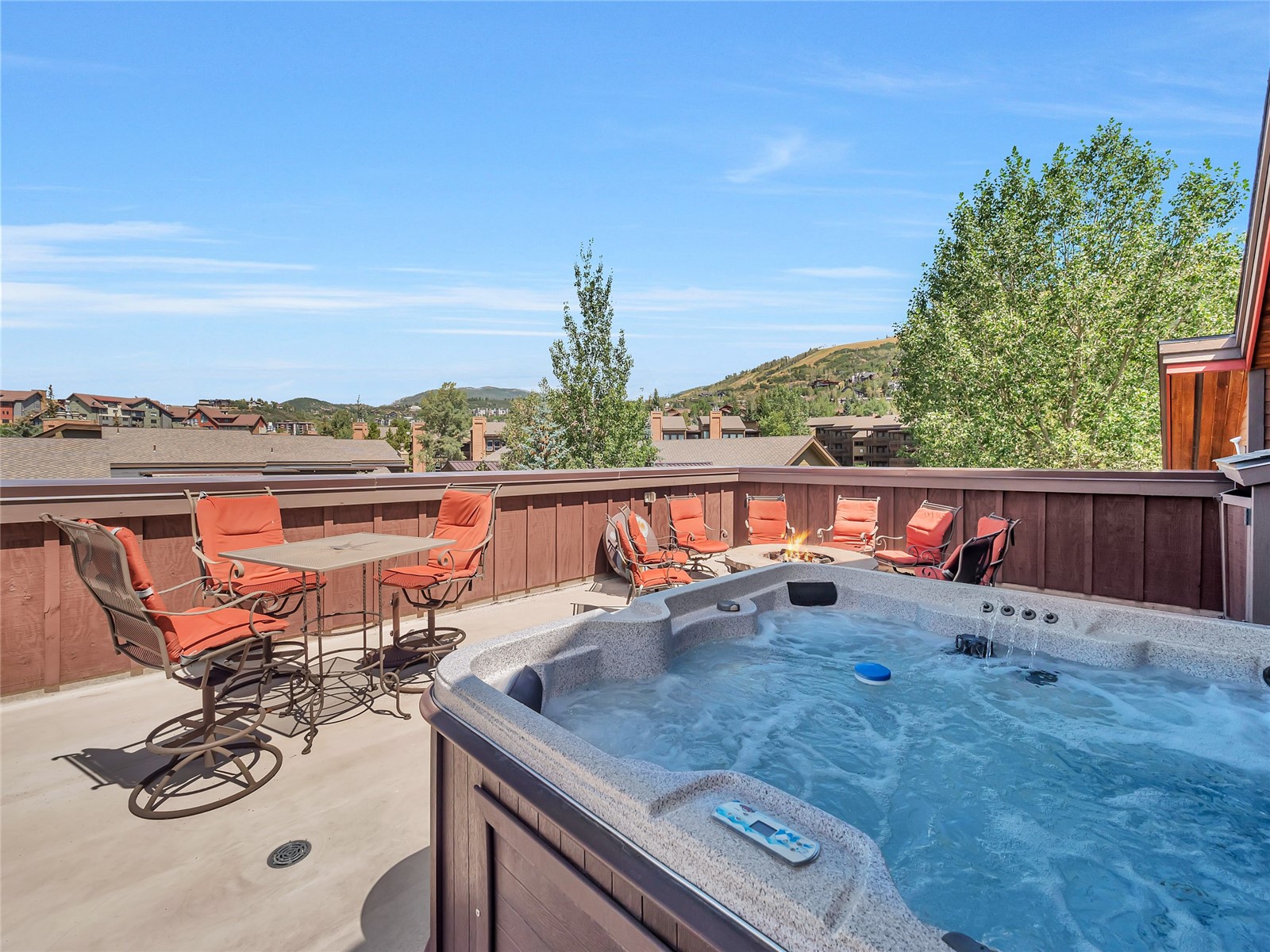 Outdoor deck with a large hot tub, orange patio chairs, and views of Steamboat Springs hills.