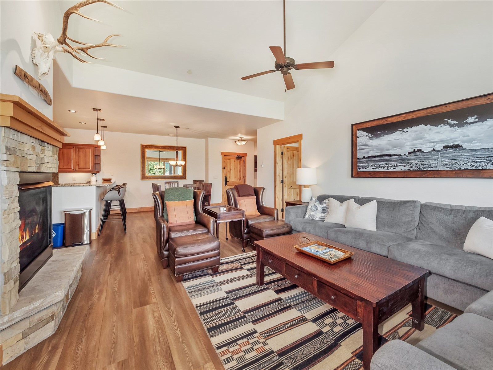 Furnished living room with a stone fireplace, gray sectional, leather armchairs, and patterned rug.