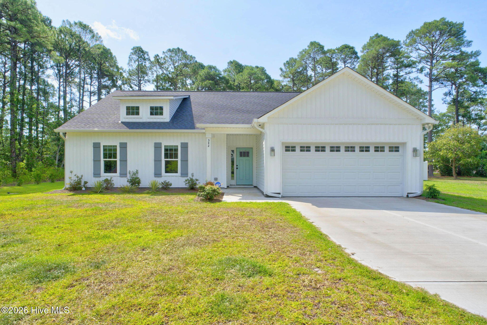 White single-story home with a pale blue-green door, wide garage, and mature trees.