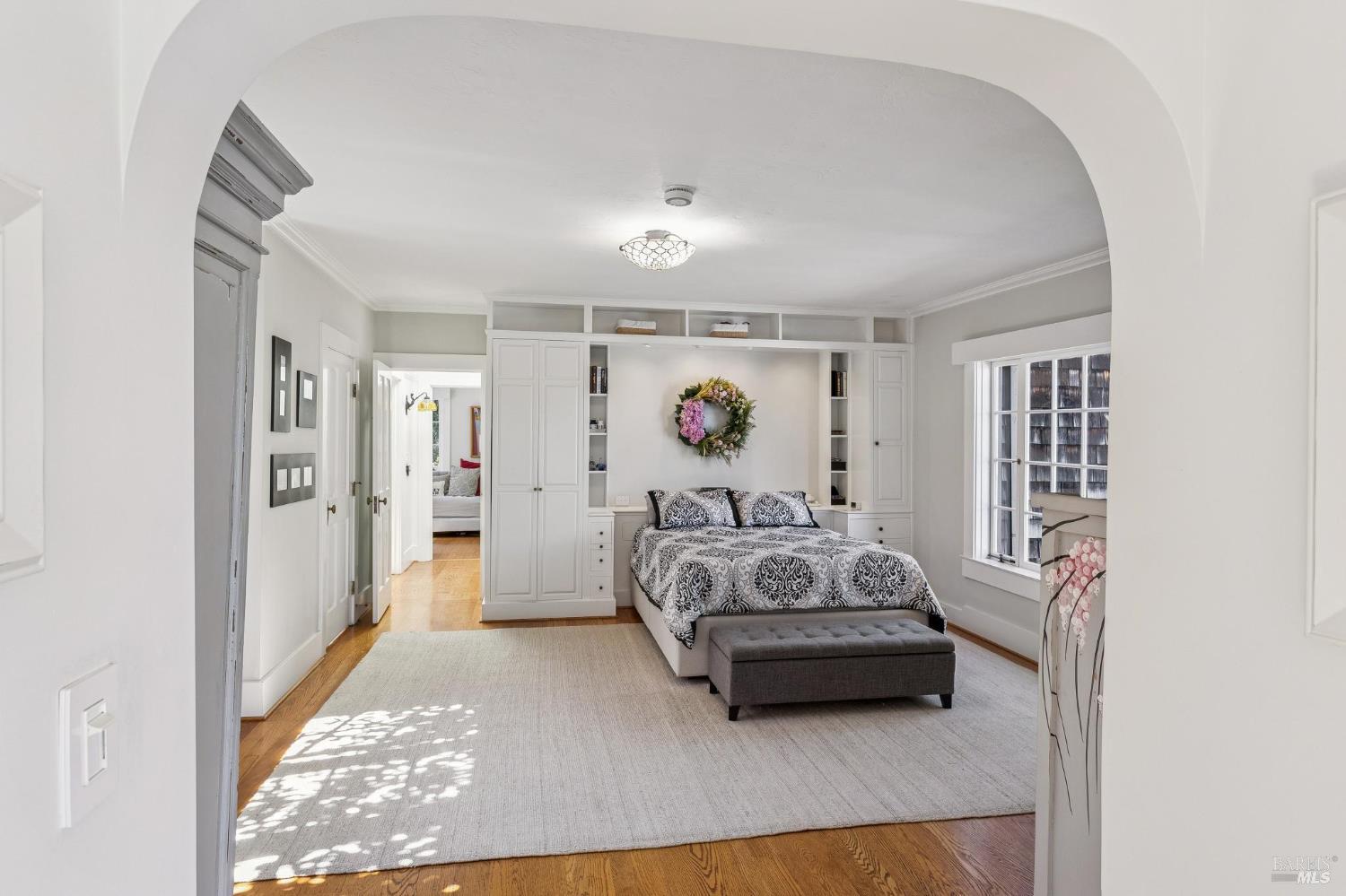 Bedroom with built-in white cabinetry, patterned bed, and a wide arched entry.