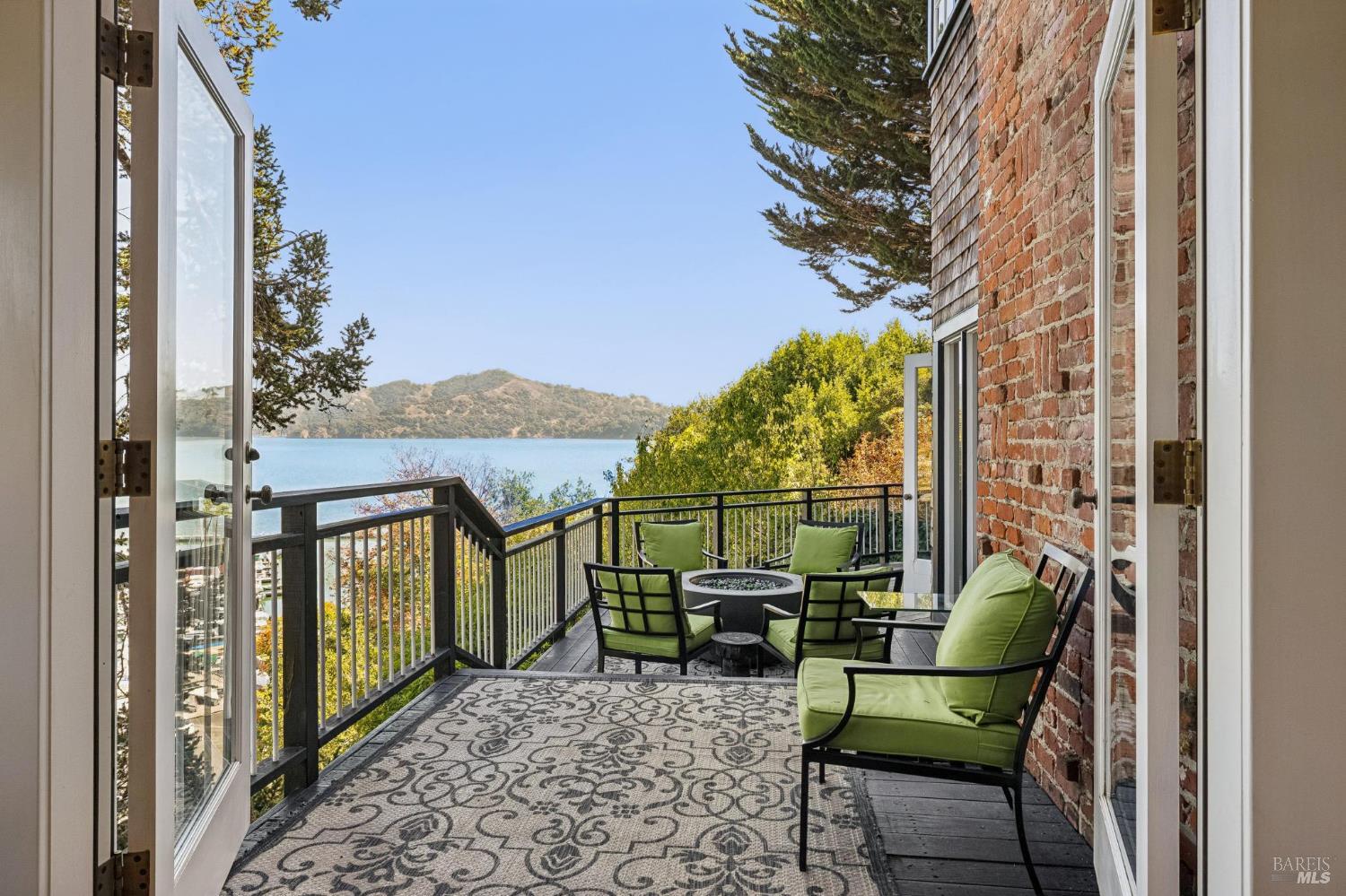 Furnished balcony with green-cushioned seating overlooking the water and hills.