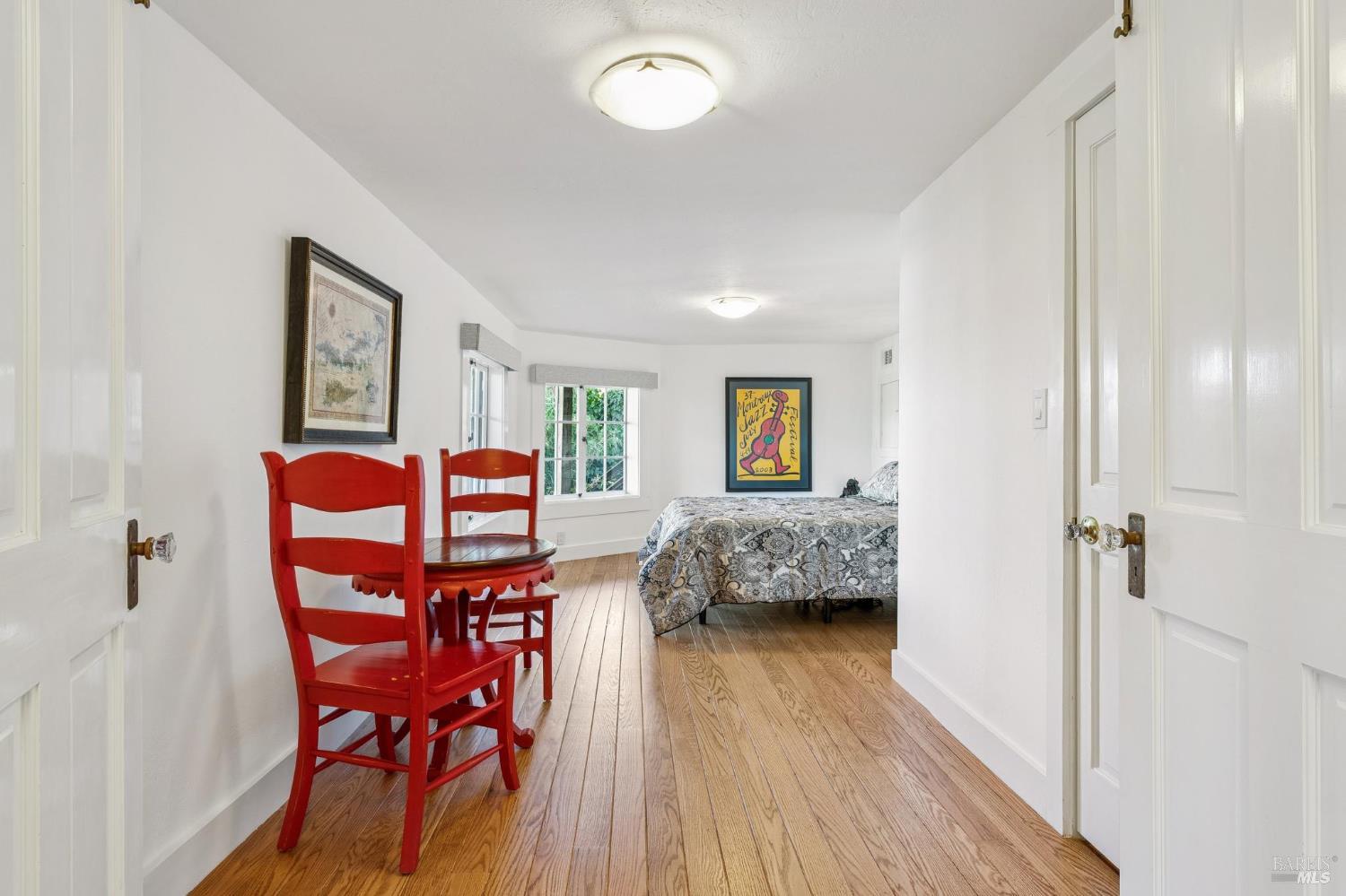 Bedroom with a patterned bedspread, red wooden chairs, and hardwood floors.