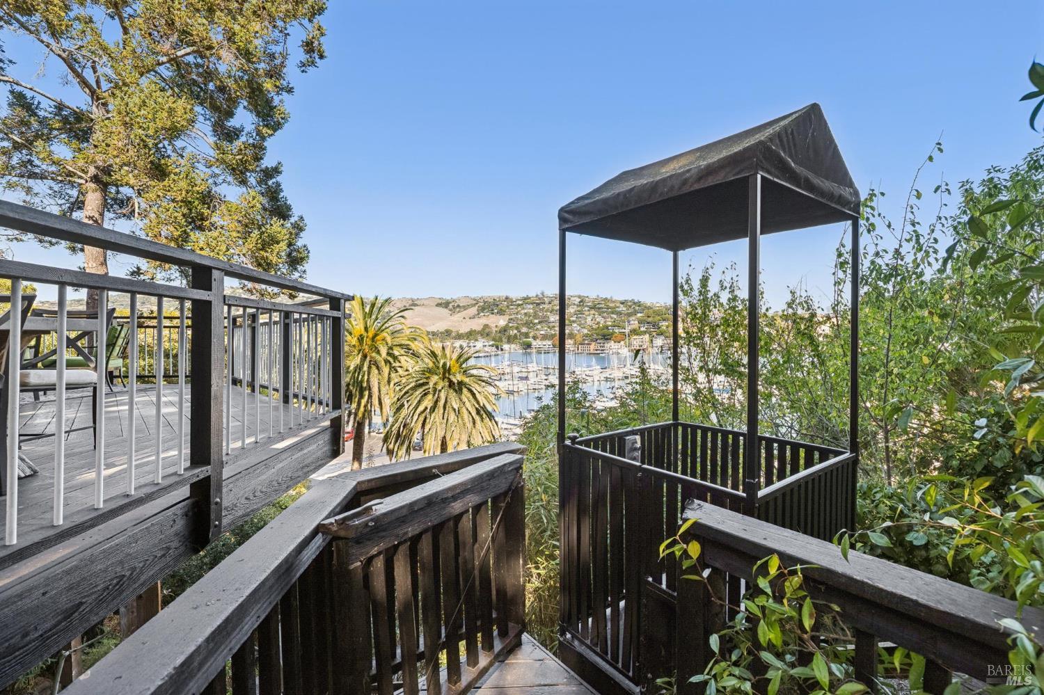Deck with black railings and canopy overlooking a marina and hillside.