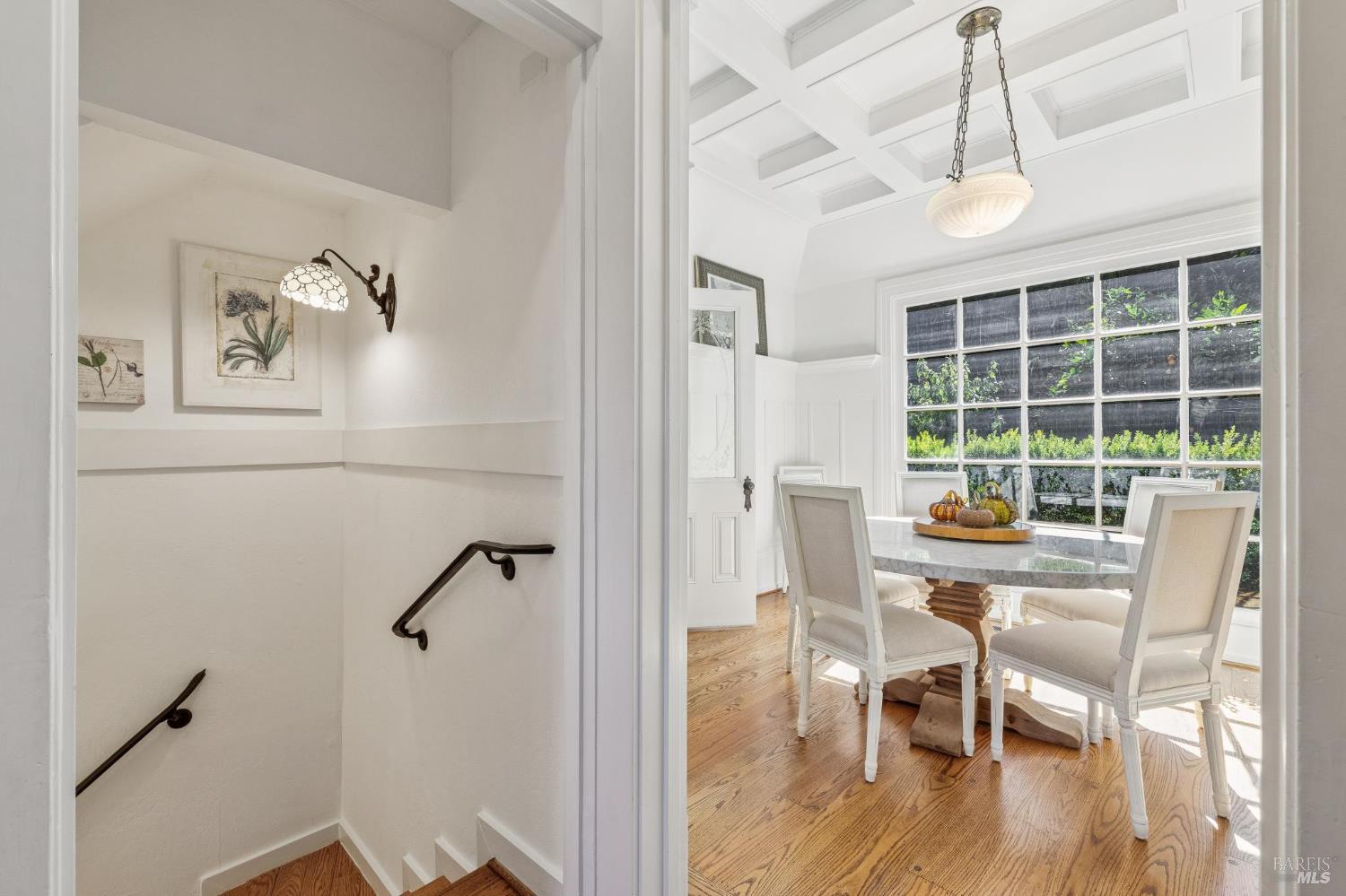 Bright dining room with a coffered ceiling, large divided-light window, and adjoining staircase.