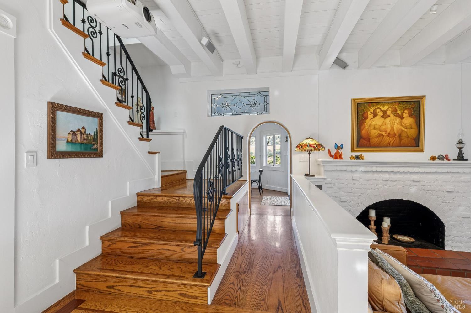 Entry hall with a curved wood staircase, ornate iron railings, and a white brick fireplace.