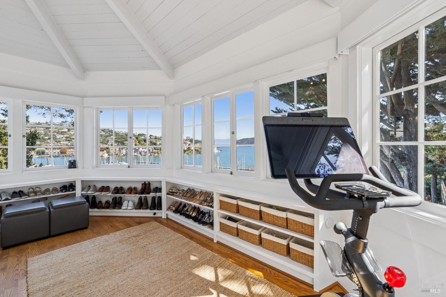Bright room with an exercise bike, shoe shelves, and windows overlooking the harbor.