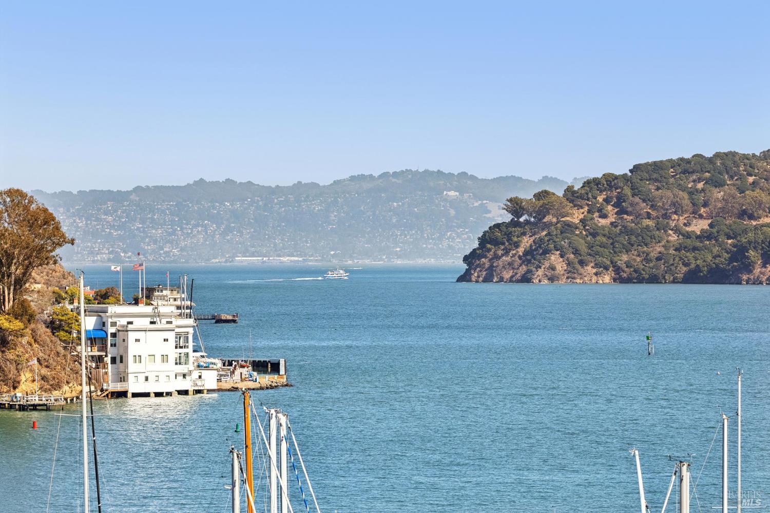 Bay view with a boat crossing between waterfront homes and wooded hills.