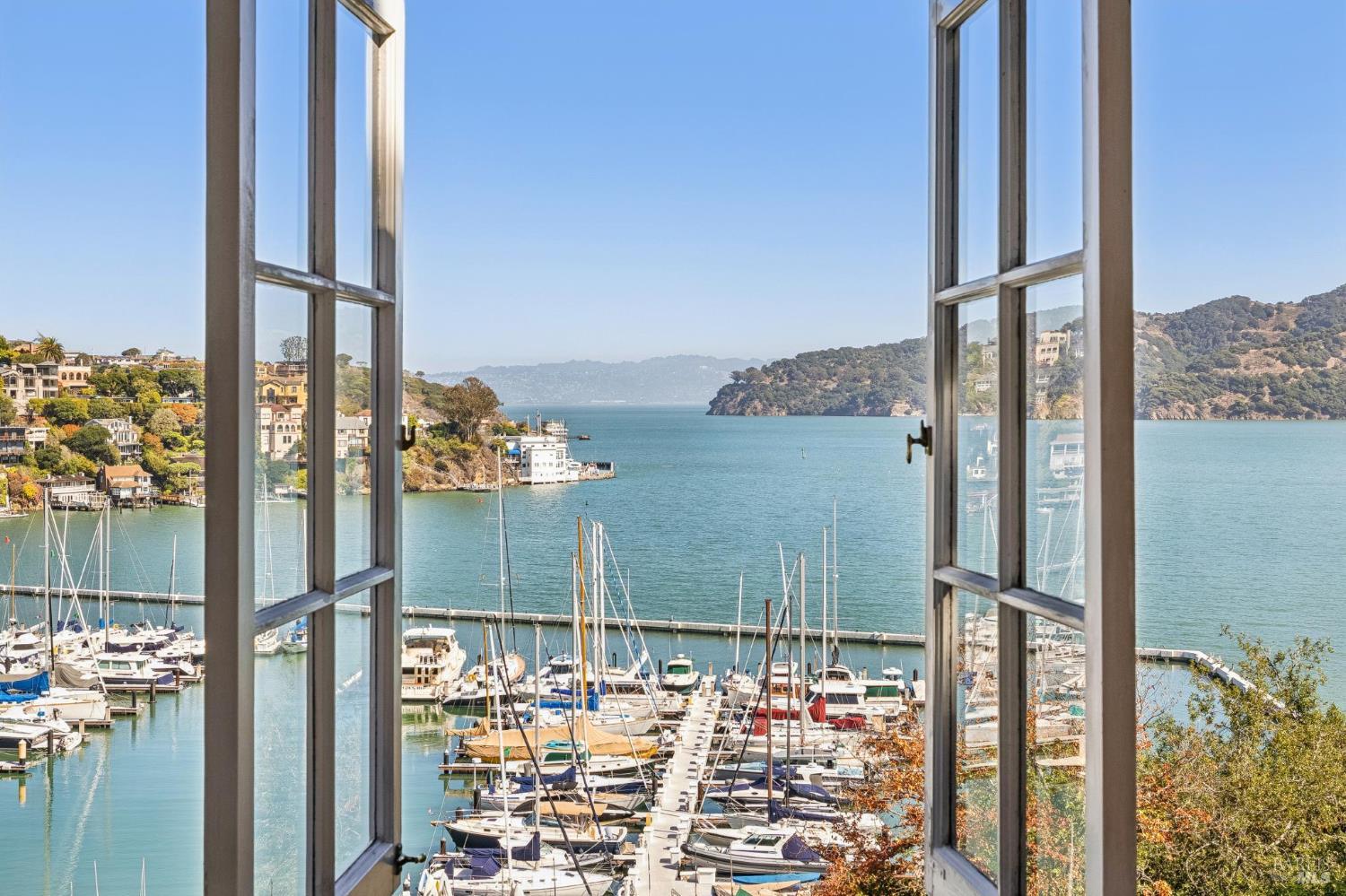 Bay and marina viewed through open windows, with boats below and wooded hills across the water.