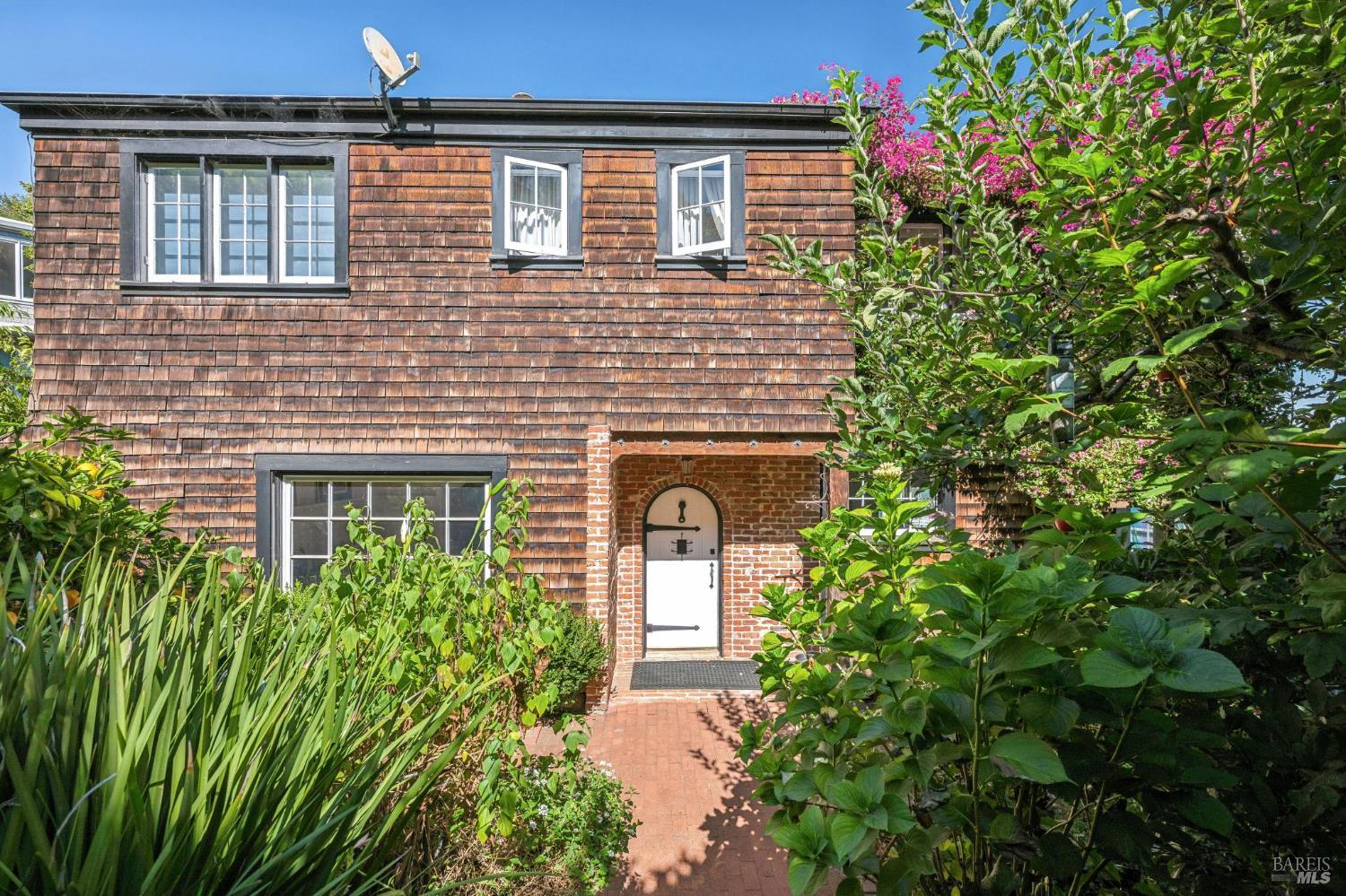 Shingle-sided home with a brick arched entry, white windows, and a leafy front garden.