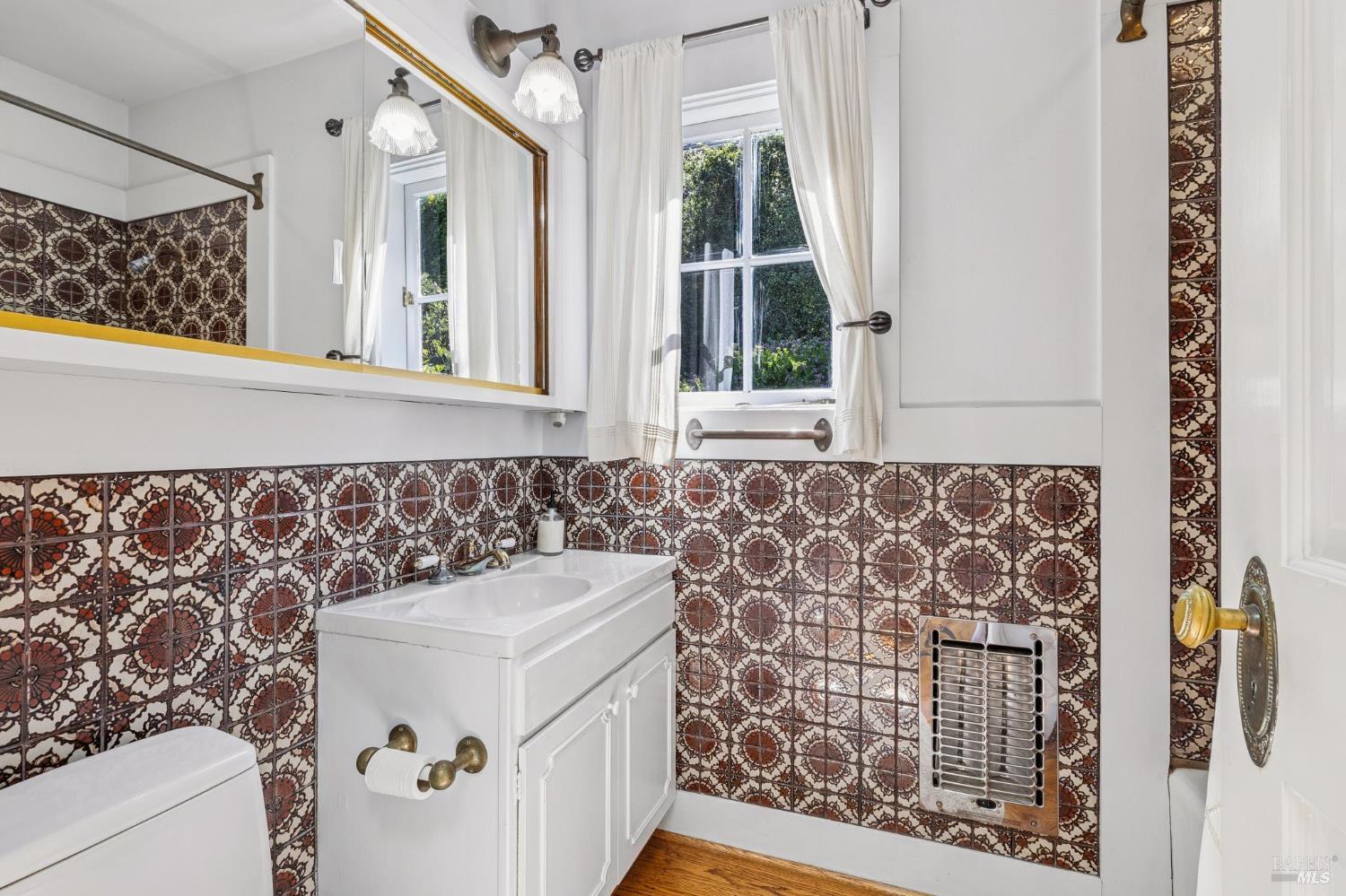 Bathroom with ornate patterned tile, a white vanity, and a curtained window.