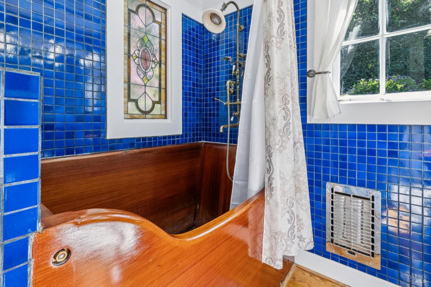 Bathroom with a polished wooden soaking tub, vivid blue tile, and stained-glass window.
