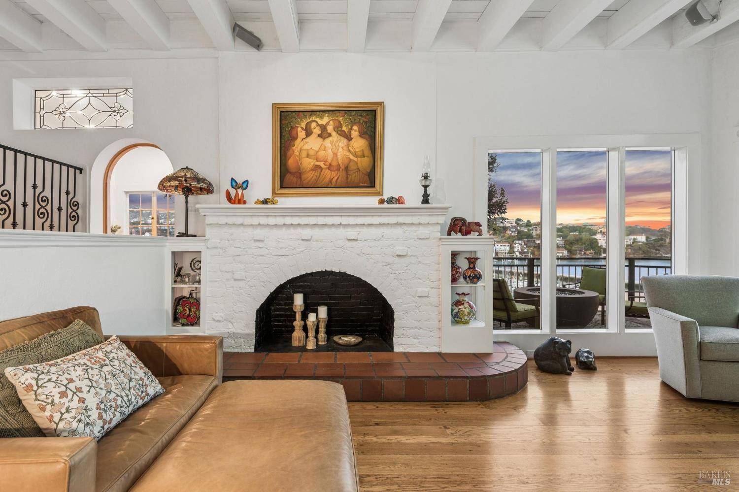 Living room with a white brick fireplace, vaulted beamed ceiling, and sunset views over the water.