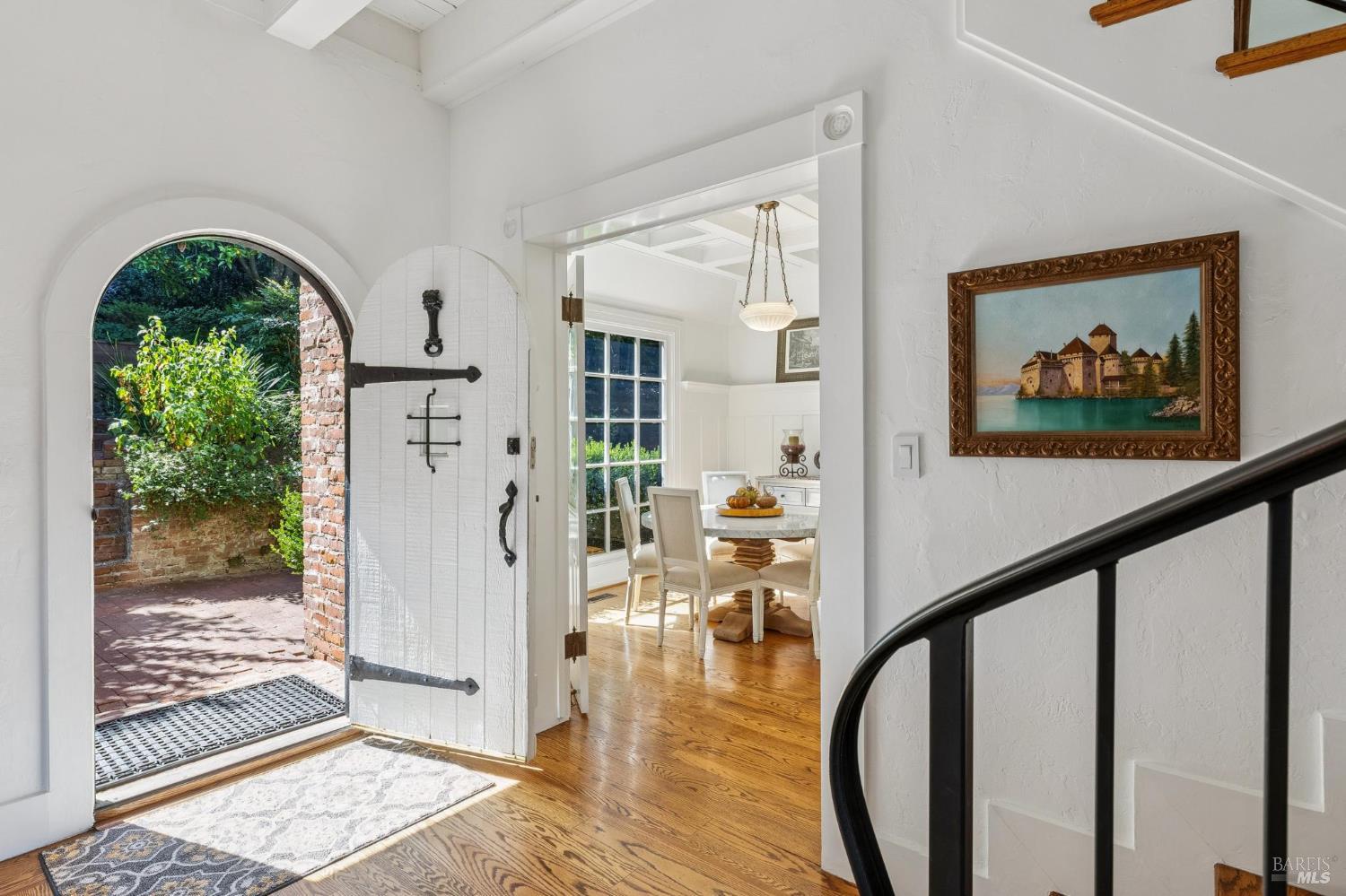 Entry hall with an arched open door to a brick patio and a staircase beside the dining room.