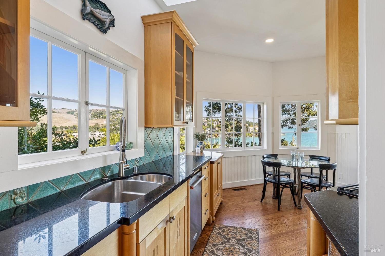 Kitchen with turquoise tile backsplash, wood cabinetry, and bay windows overlooking the water.