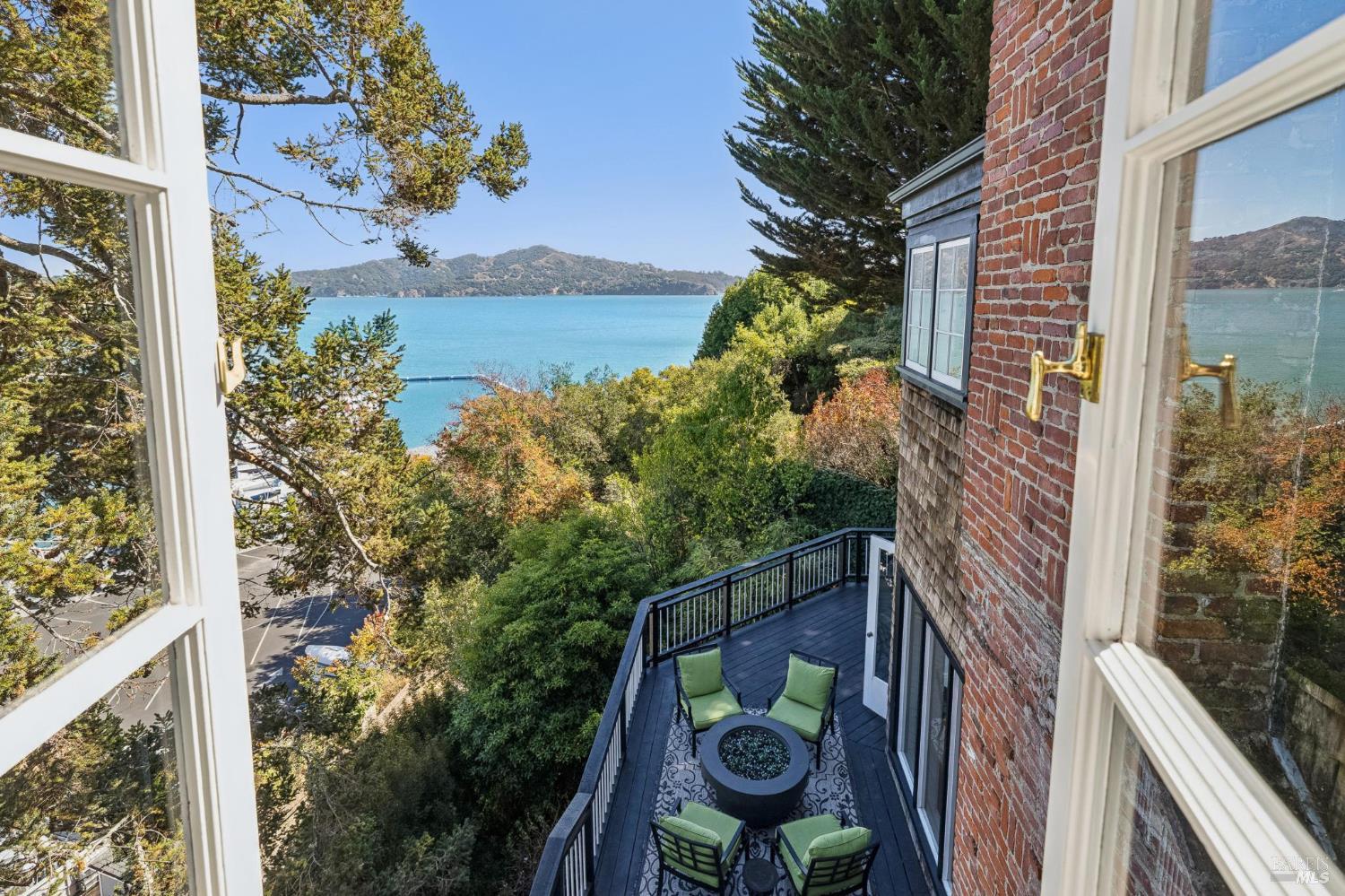 Deck with green seating overlooks a blue bay, framed by open windows and brick walls.