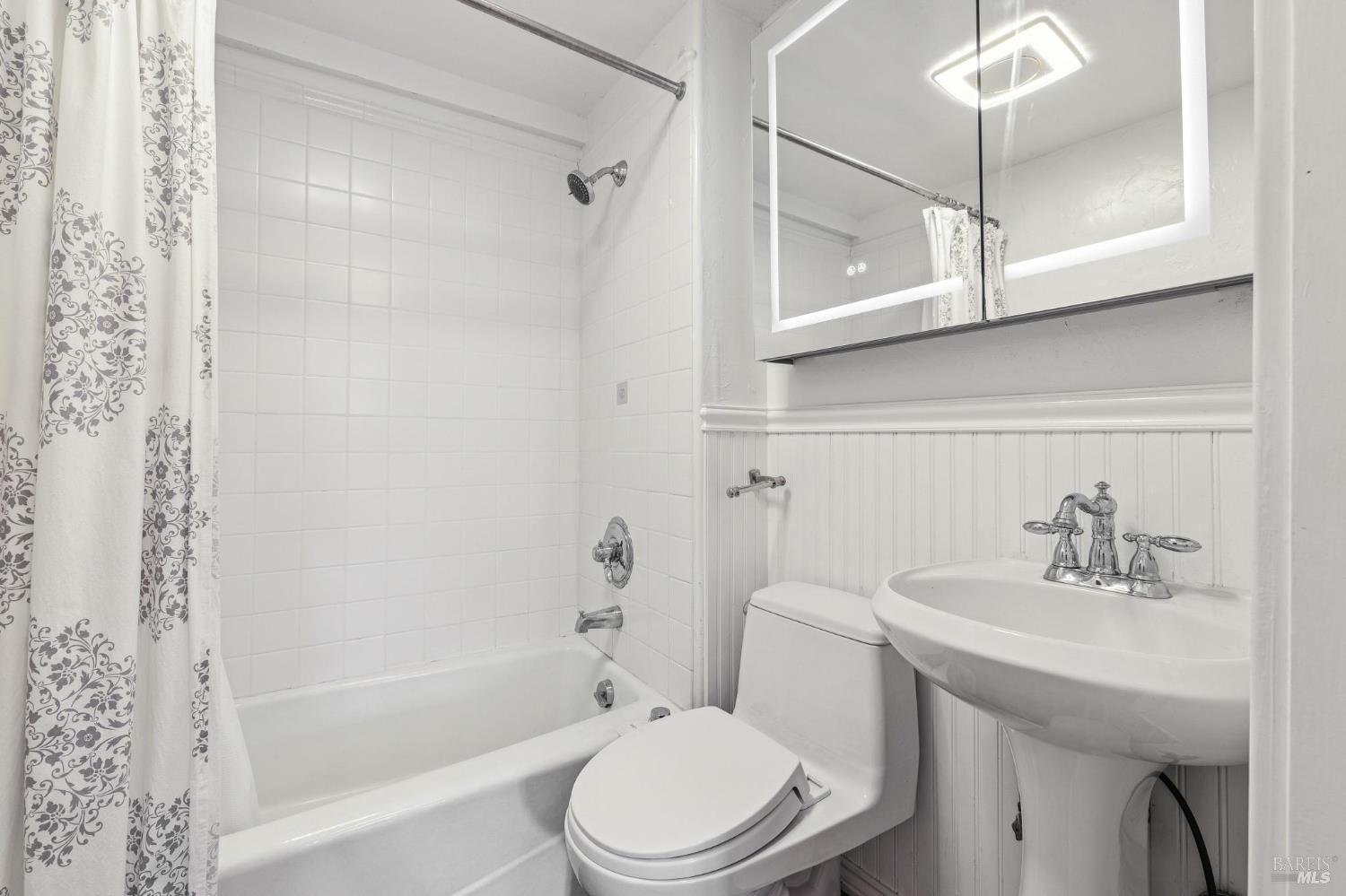 White bathroom with a tiled tub and shower, pedestal sink, and mirrored cabinet.