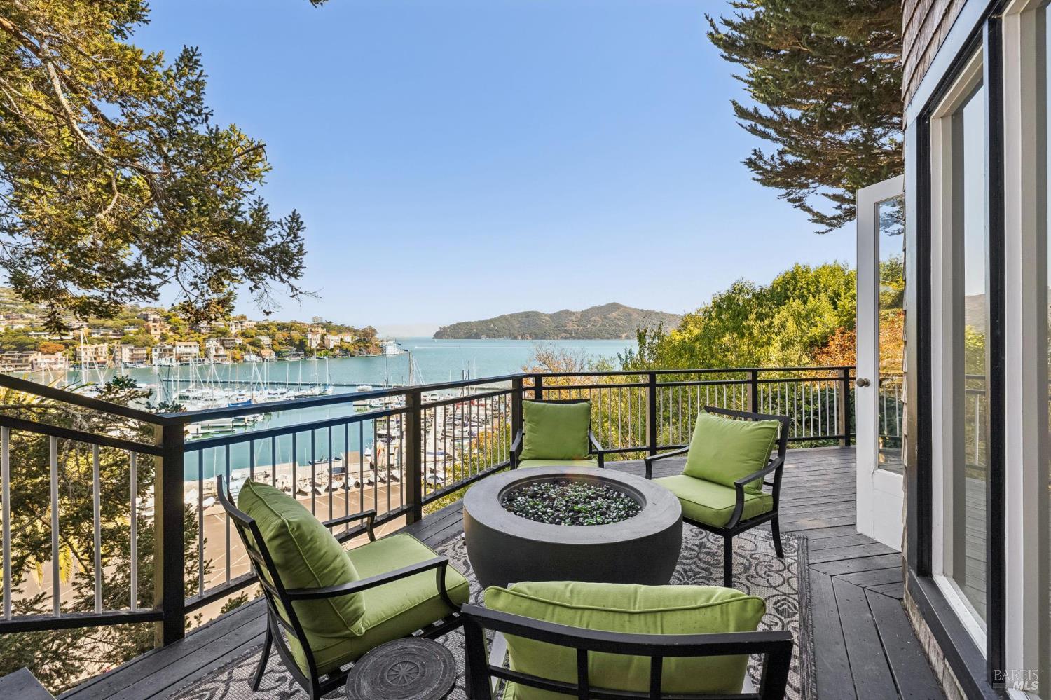 Furnished deck with green lounge chairs and a fire pit overlooking a marina and bay.