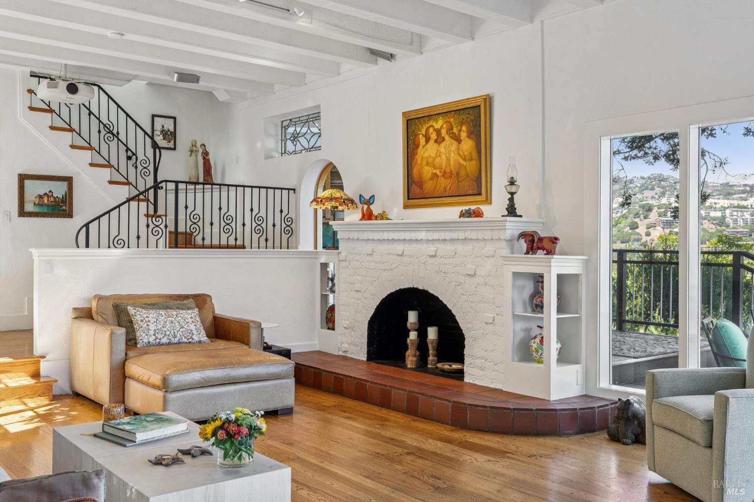 Living room with a white brick fireplace, spiral staircase, and glass doors opening to a hillside view.