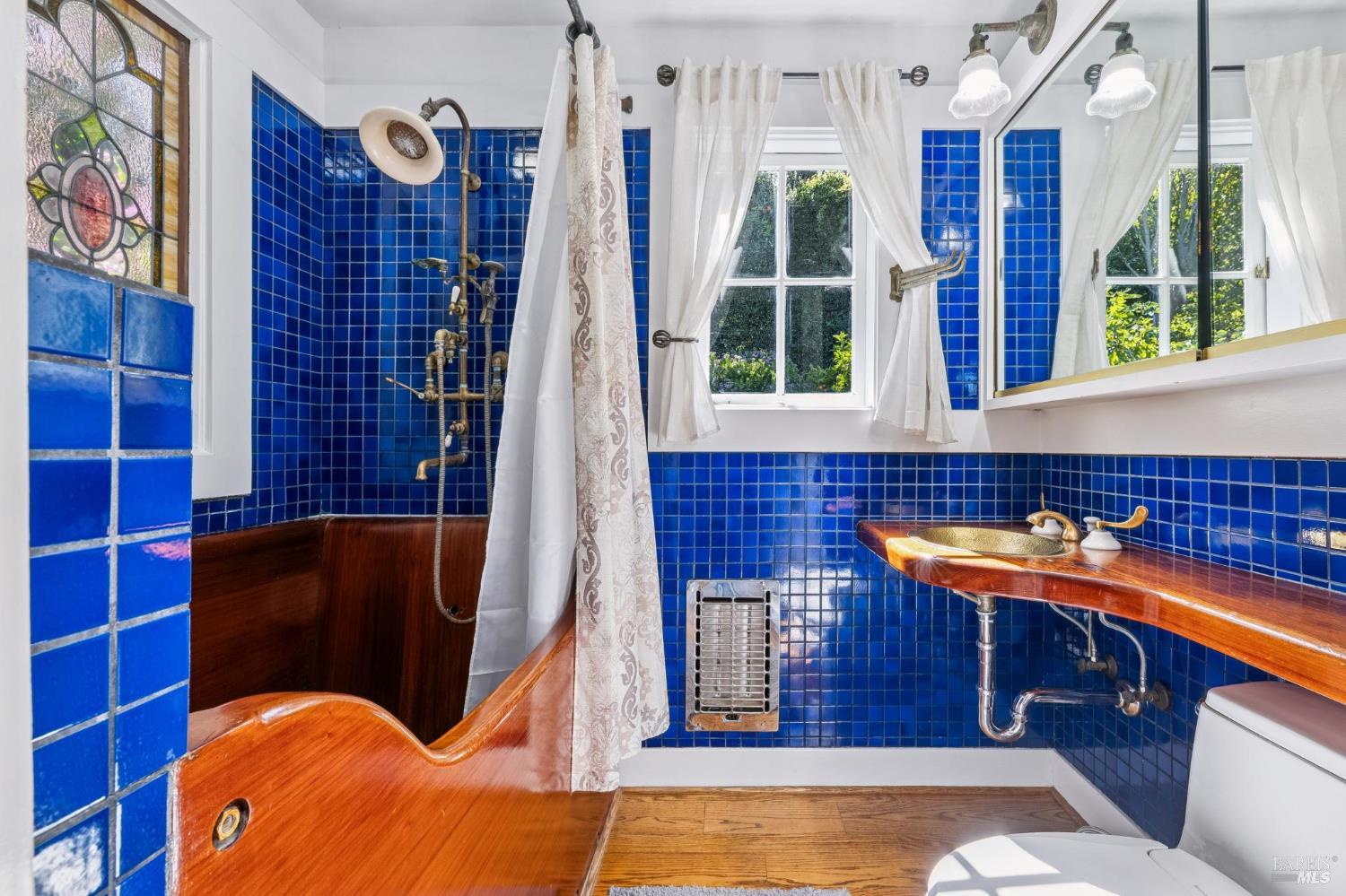 Bathroom with vivid blue tile, a sculpted wooden tub, and stained-glass window.