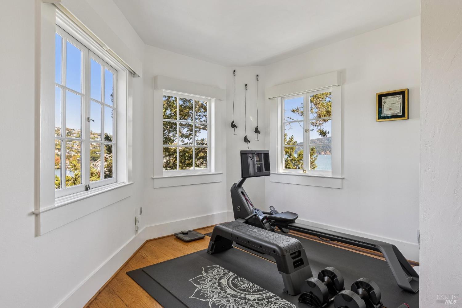 Home gym with exercise equipment, hardwood floors, and windows overlooking the water.