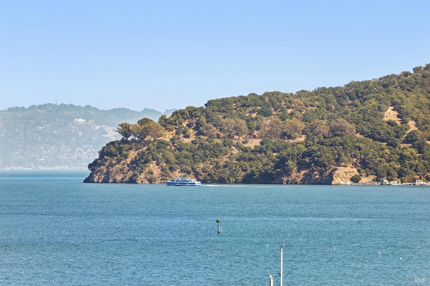Bay view with a wooded peninsula and a passenger boat crossing the water.