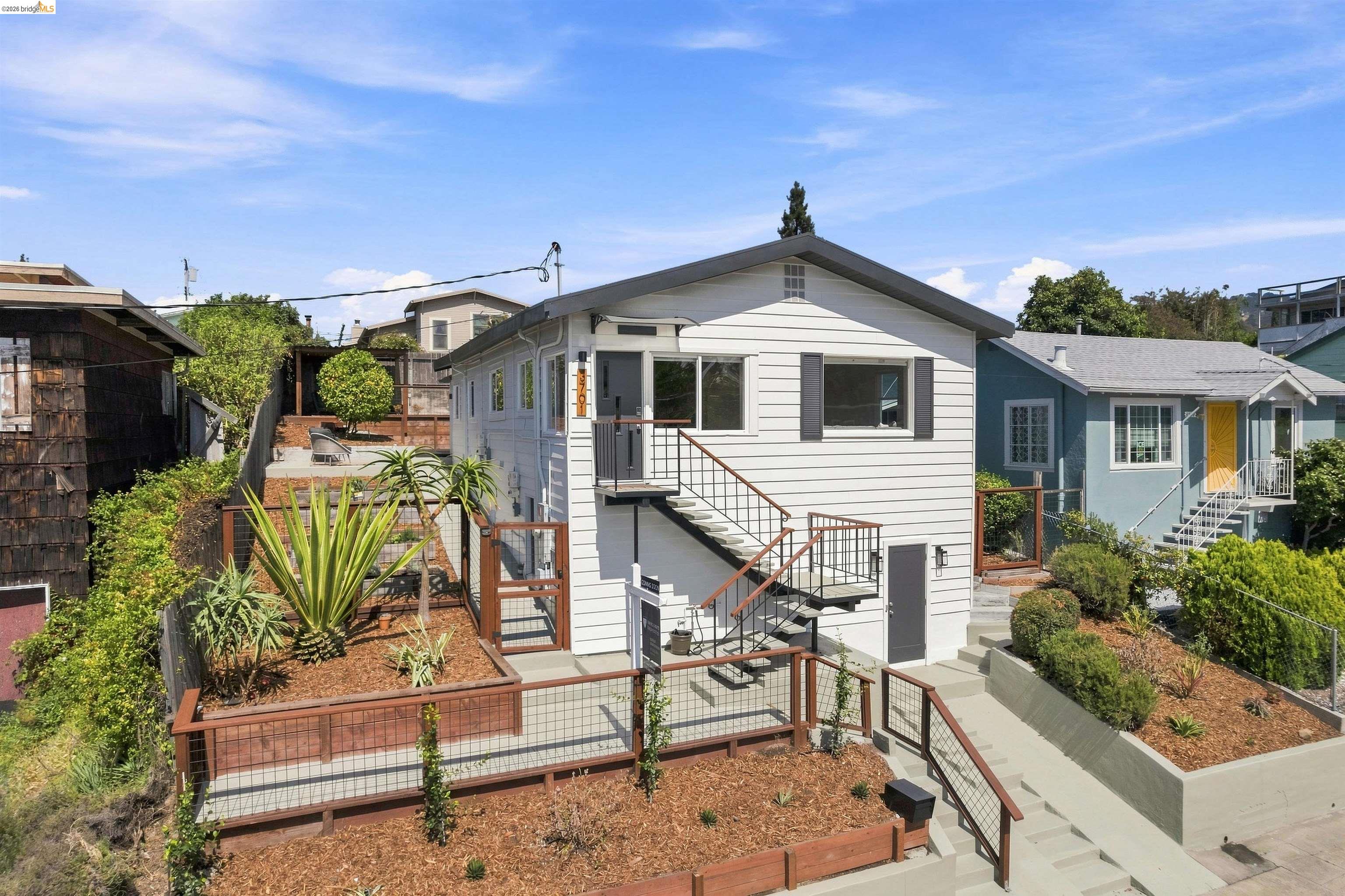White Oakland home with a gabled roof, landscaped raised beds, and multiple outdoor stairways.