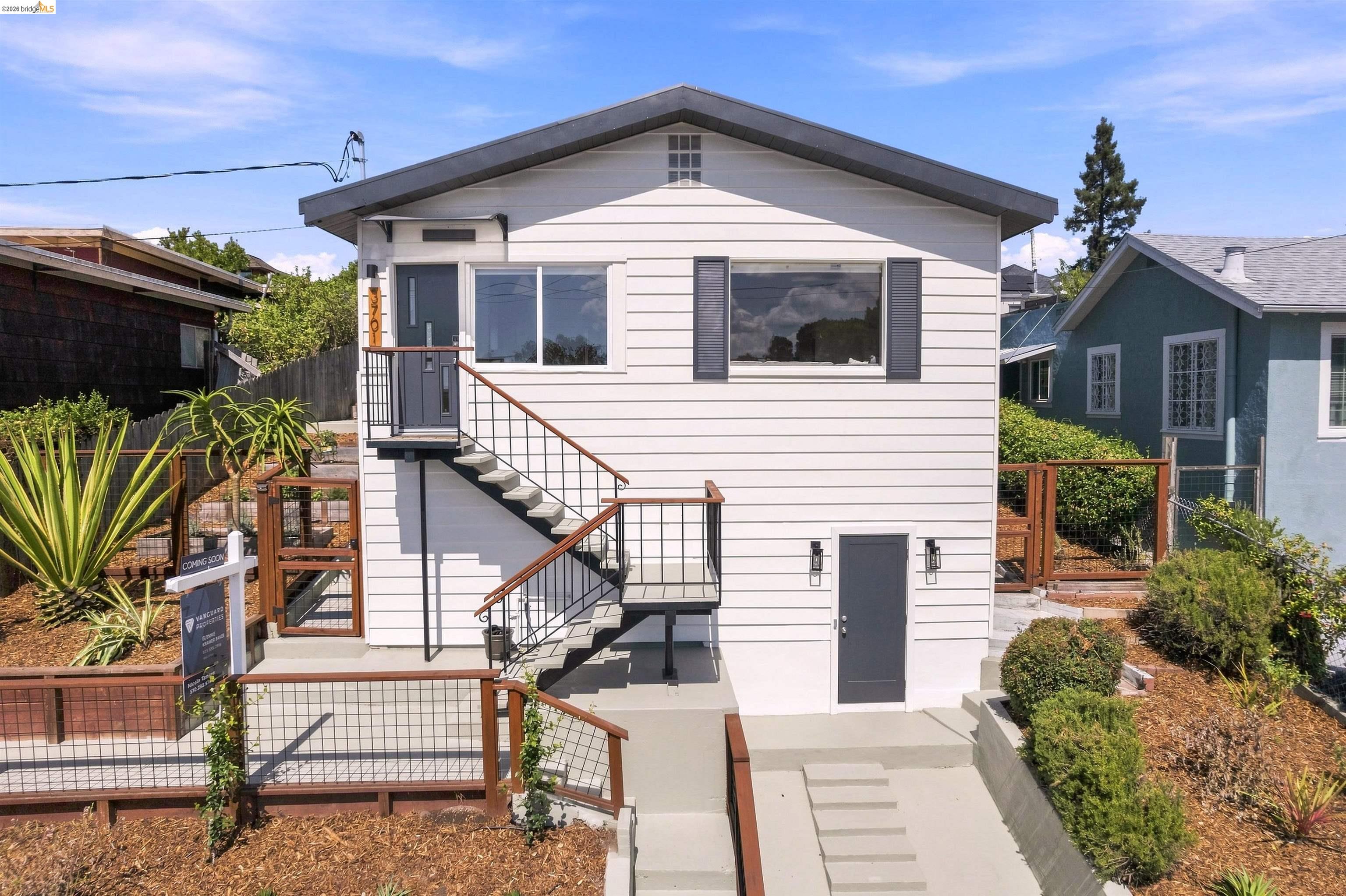 White gabled home with large front windows, exterior stairs, and wood-and-wire fencing.