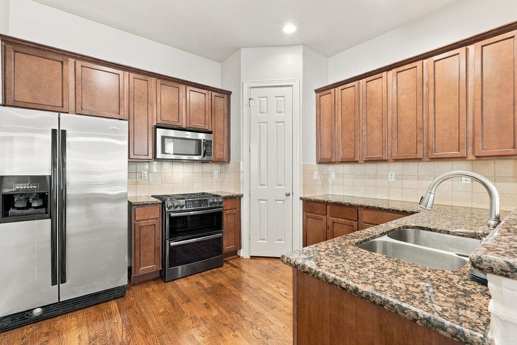 Kitchen with wood cabinets, granite counters, stainless steel appliances, and hardwood floors.