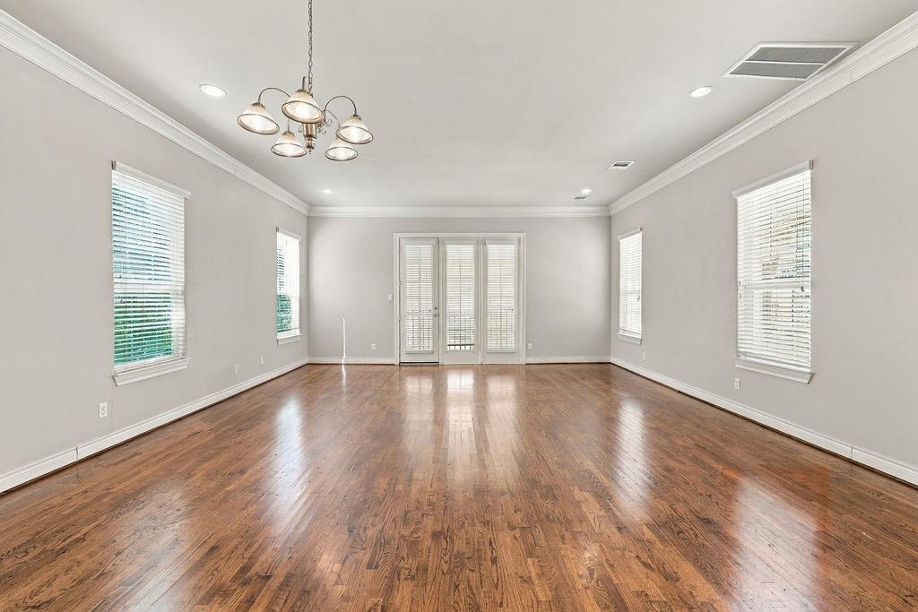 Empty room with polished hardwood floors, a chandelier, several windows, and glass-paneled doors.