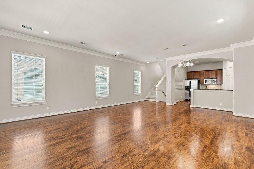 Unfurnished living area with hardwood floors, three windows, and an adjoining kitchen and staircase.