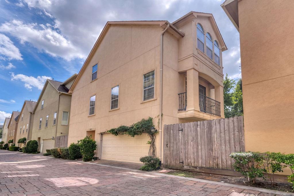 Beige multi-story townhome with an attached garage, arched windows, and a wooden privacy fence.