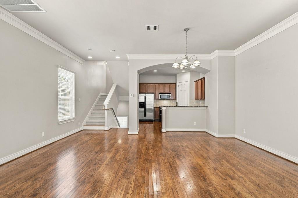Unfurnished living area with hardwood floors, staircase, and kitchen beyond an arched opening.