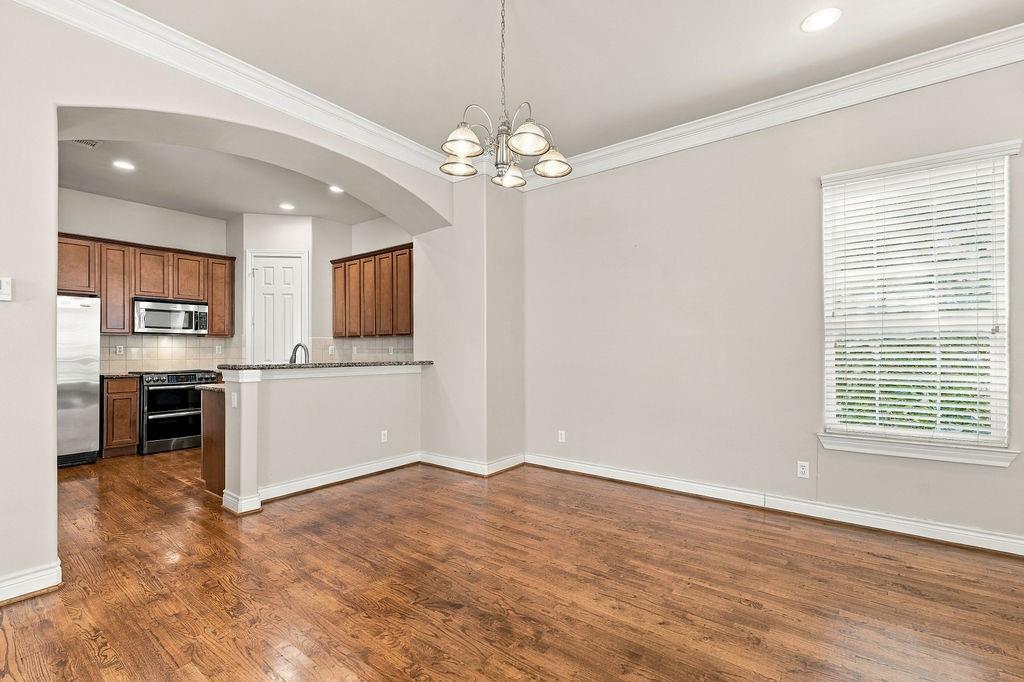 Empty dining area with hardwood floors and chandelier beside a kitchen with wood cabinets and stainless steel appliances.